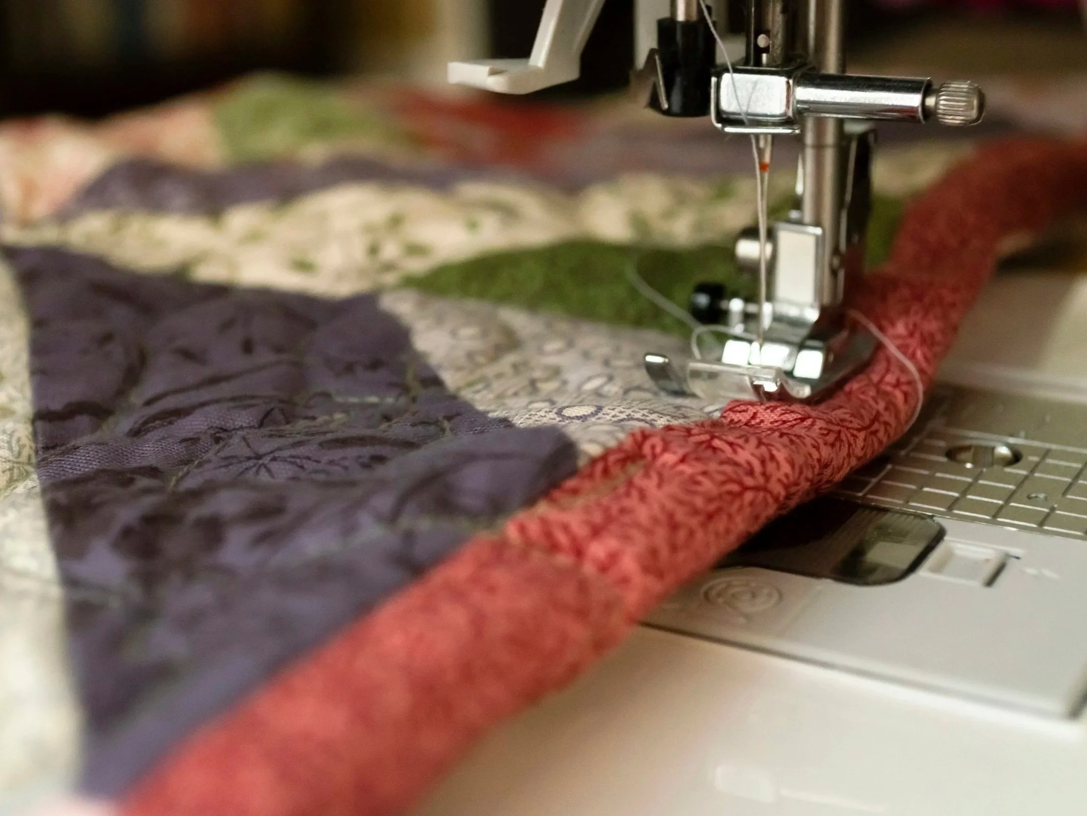 Quilt beneath a sewing machine needle and foot.
