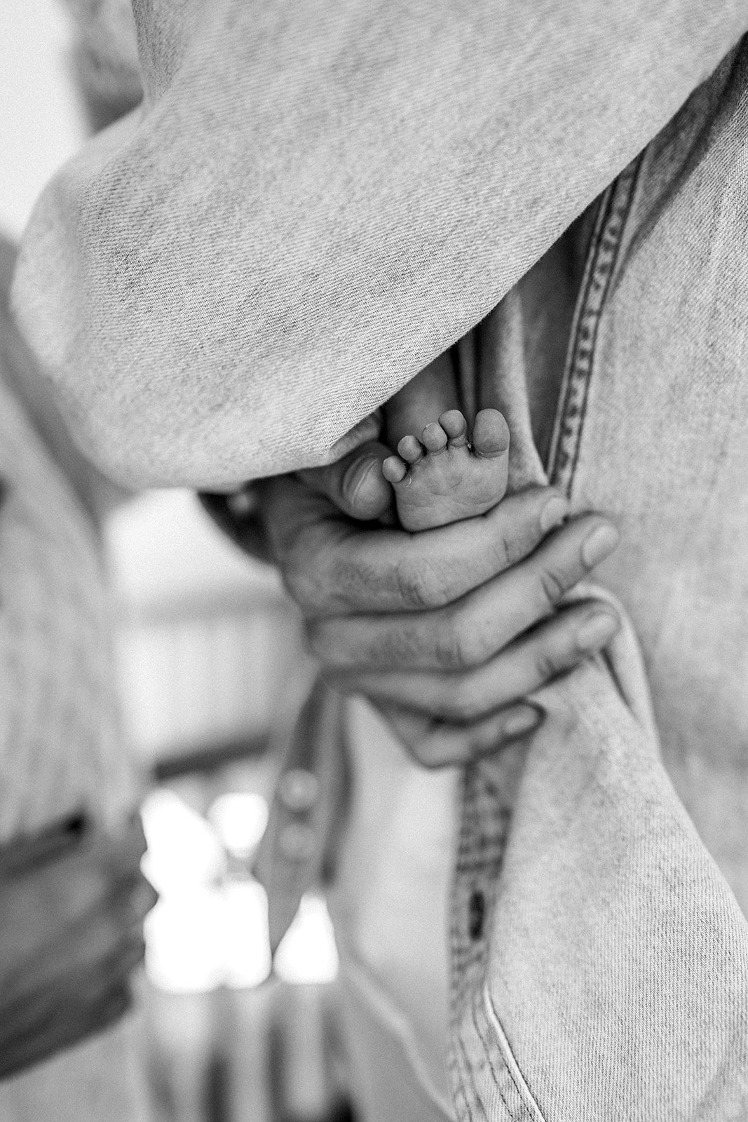 Close-up of a tiny baby hand grasping an adult's finger, with the adult cradling the baby's hand gently.