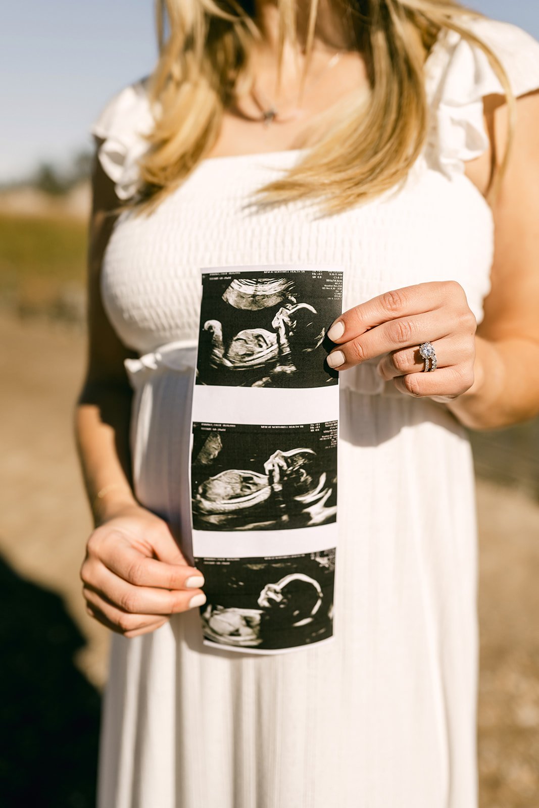 Woman holding ultrasound pictures outdoors in sunlight.