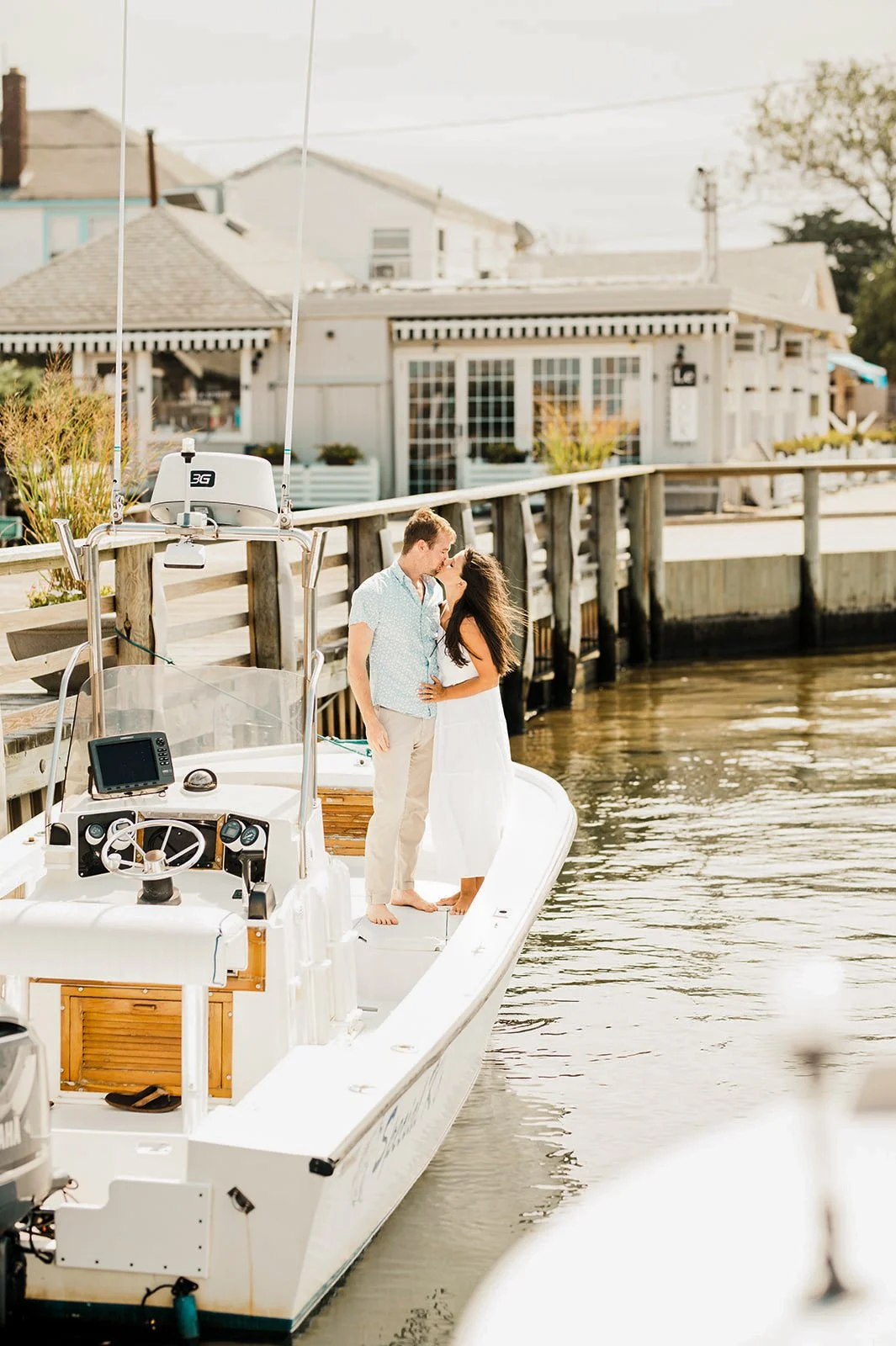 Couple kissing on a boat docked at a pier near houses during daylight.