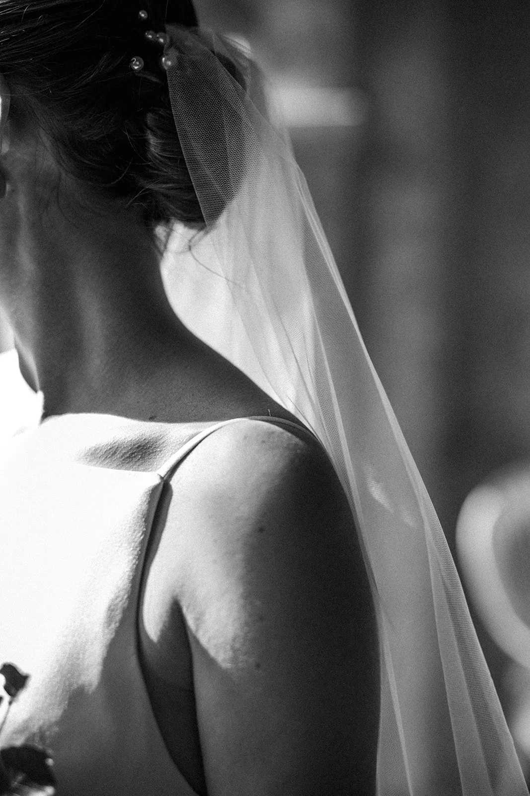 Black and white photo of a woman wearing a wedding dress and a veil, captured from behind.