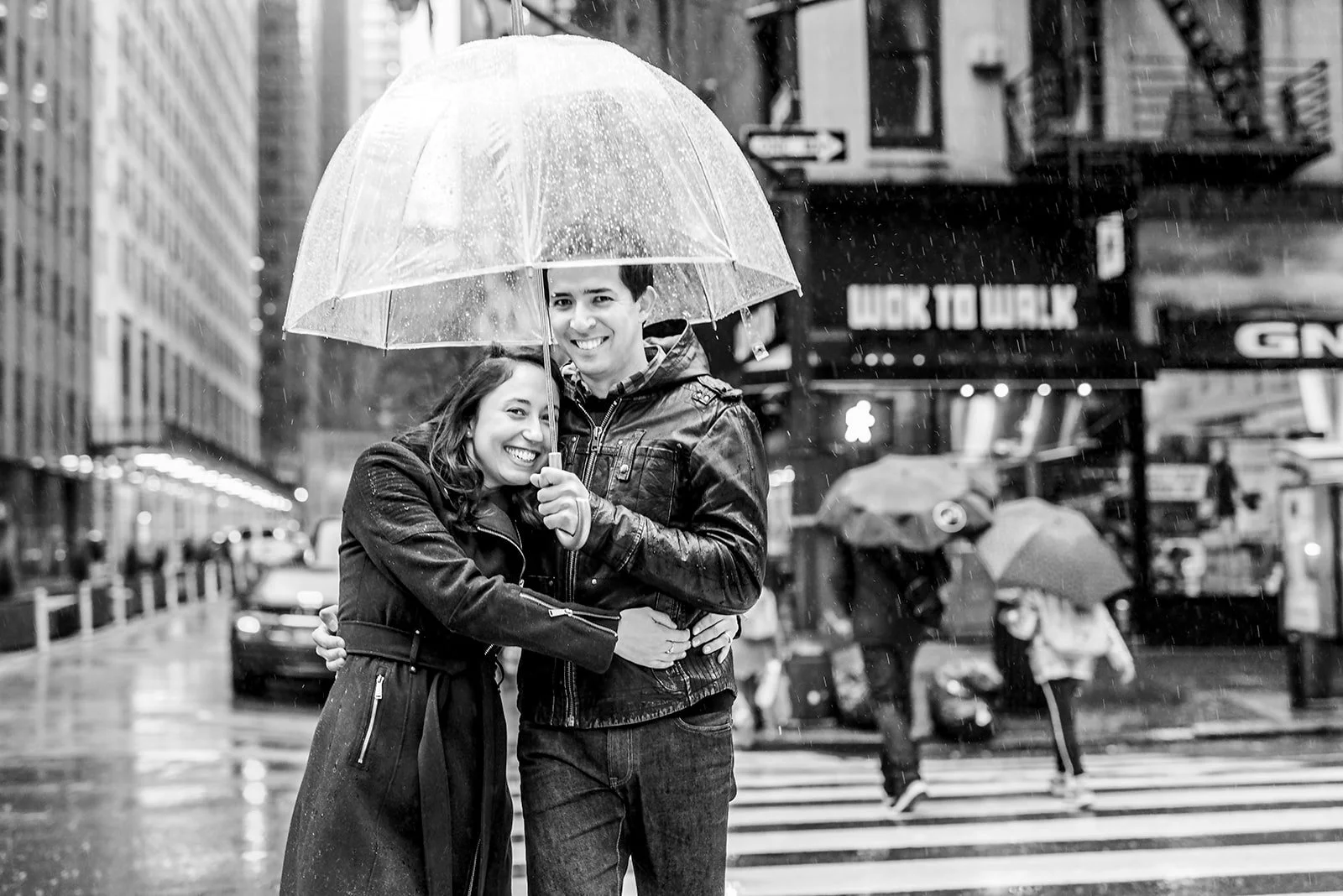 A smiling couple using an umbrella on a rainy day in a busy city street.