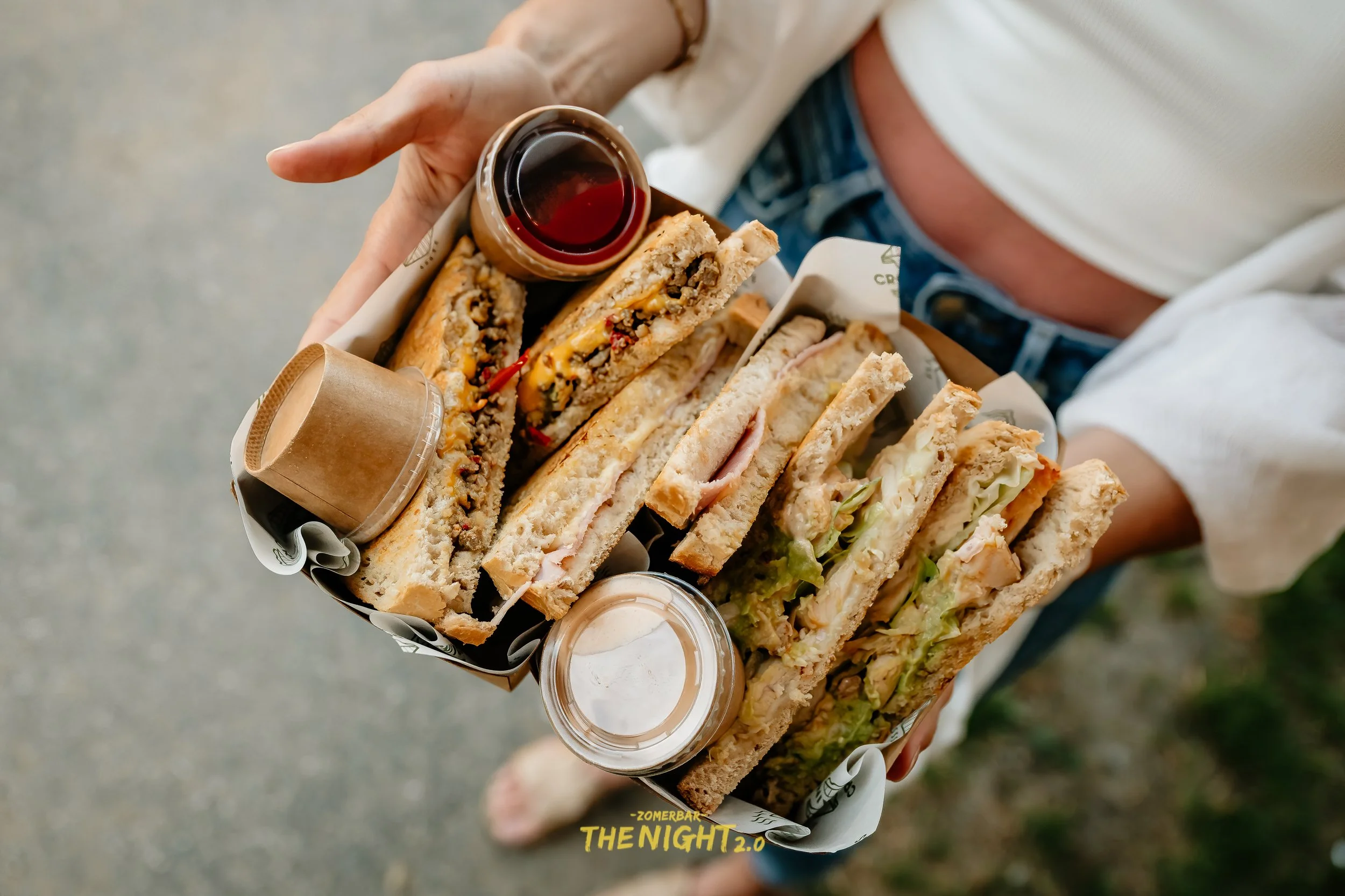 Person's hand receiving several tacos filled with seafood and garnished with lime wedges from another person at a food stall.