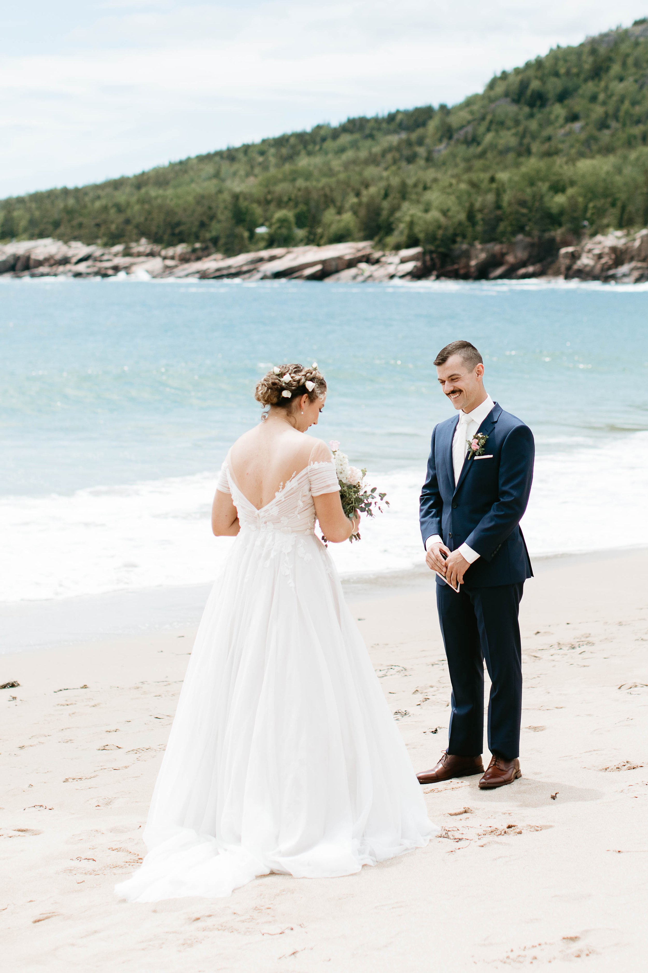   This is an image of a wedding couple standing on Sand Beach in Acadia national park during their elopement. They are facing each other reading their vows.  