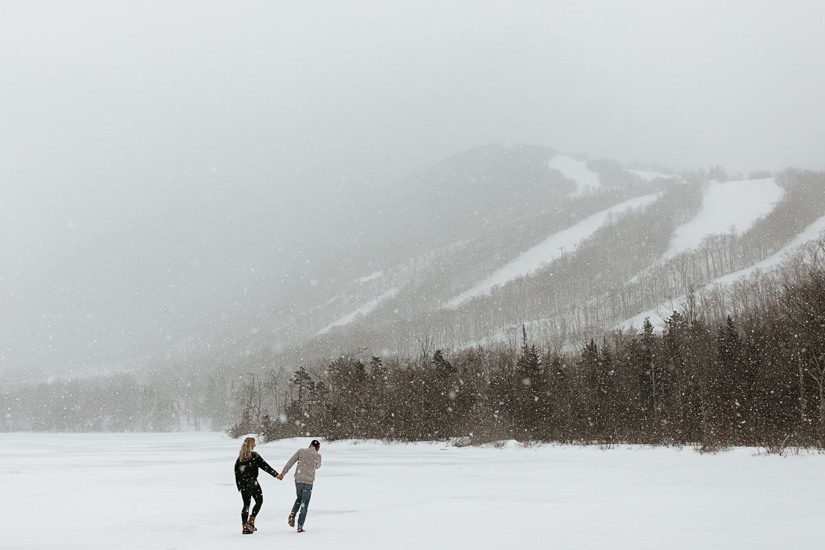 A couple runs across a frozen Echo Lake during a cold and snowy engagement session in New Hampshire 