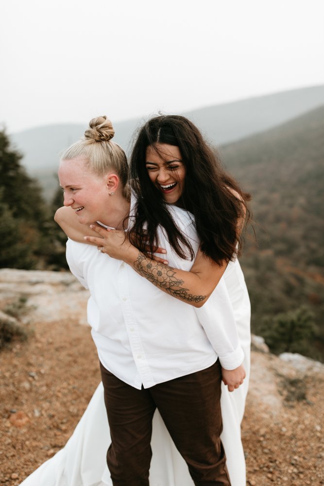  A same sex lesbian couple laughs and poses for their elopement photos in Acadia National Park on a misty fall day 
