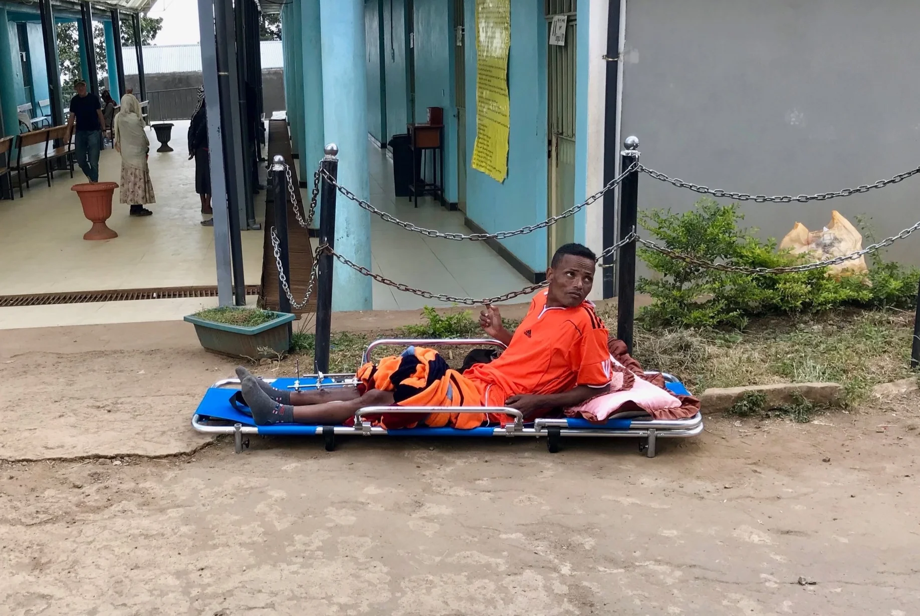 A young man waits outside the outpatient services area of the hospital. Notice the pins in his right leg.