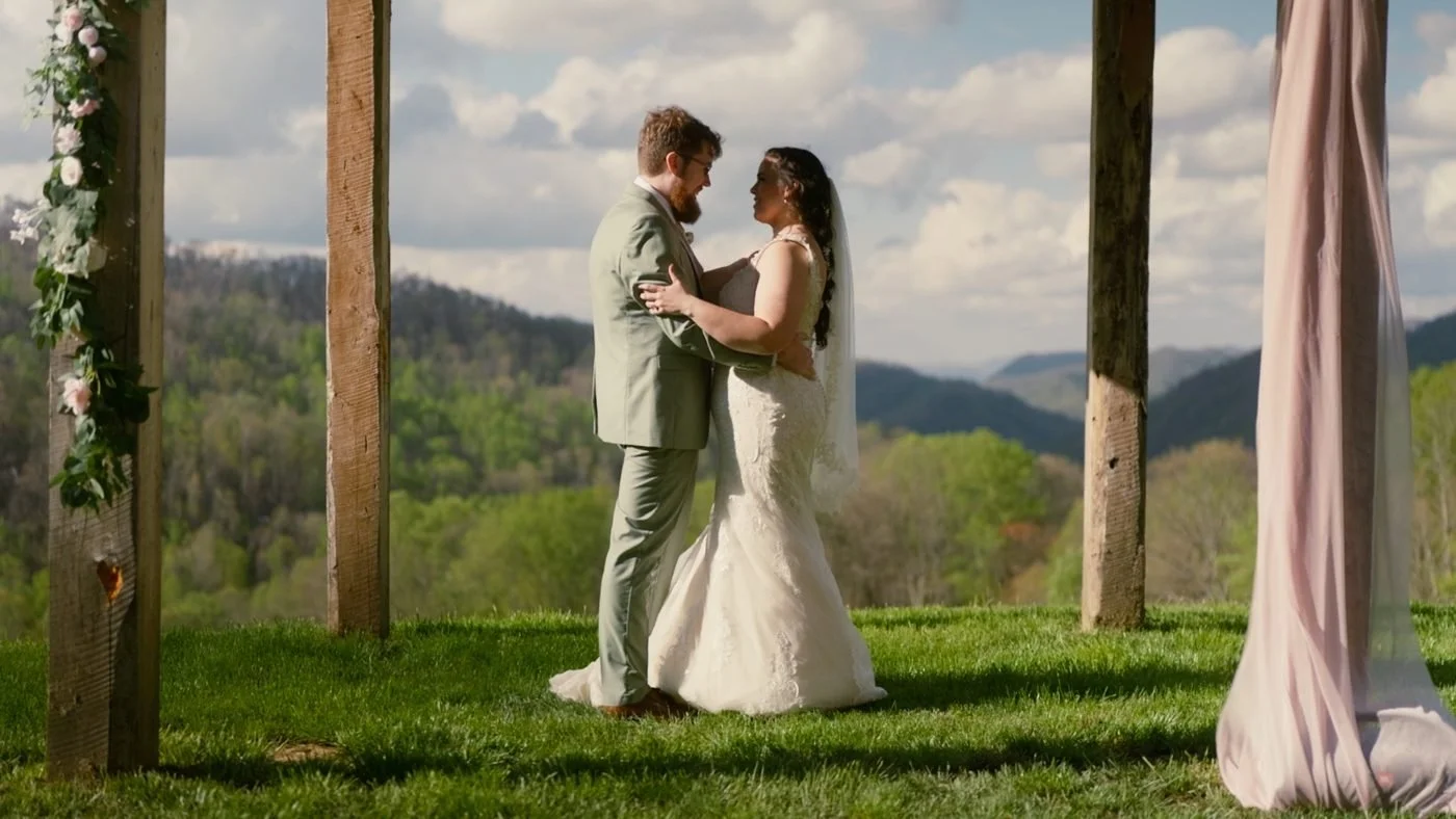 A couple dancing under a wooden pergola with mountains behind