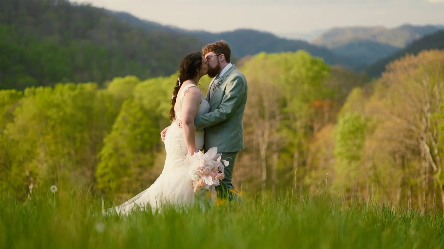 A couple kissing on a green hillside with Blue Ridge mountains behind them