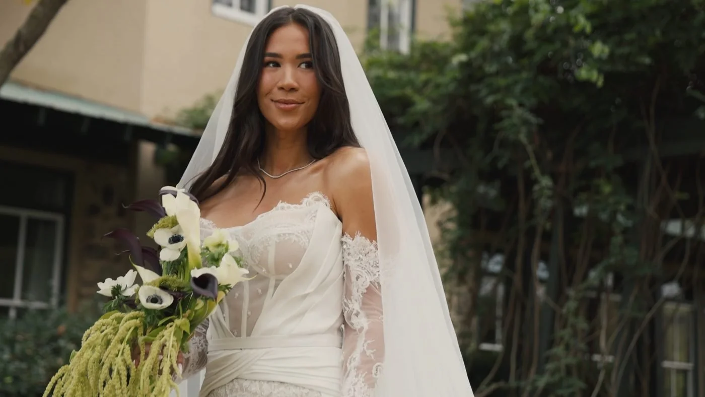 A smiling bride in a long veil holding white anemones and calla lilies