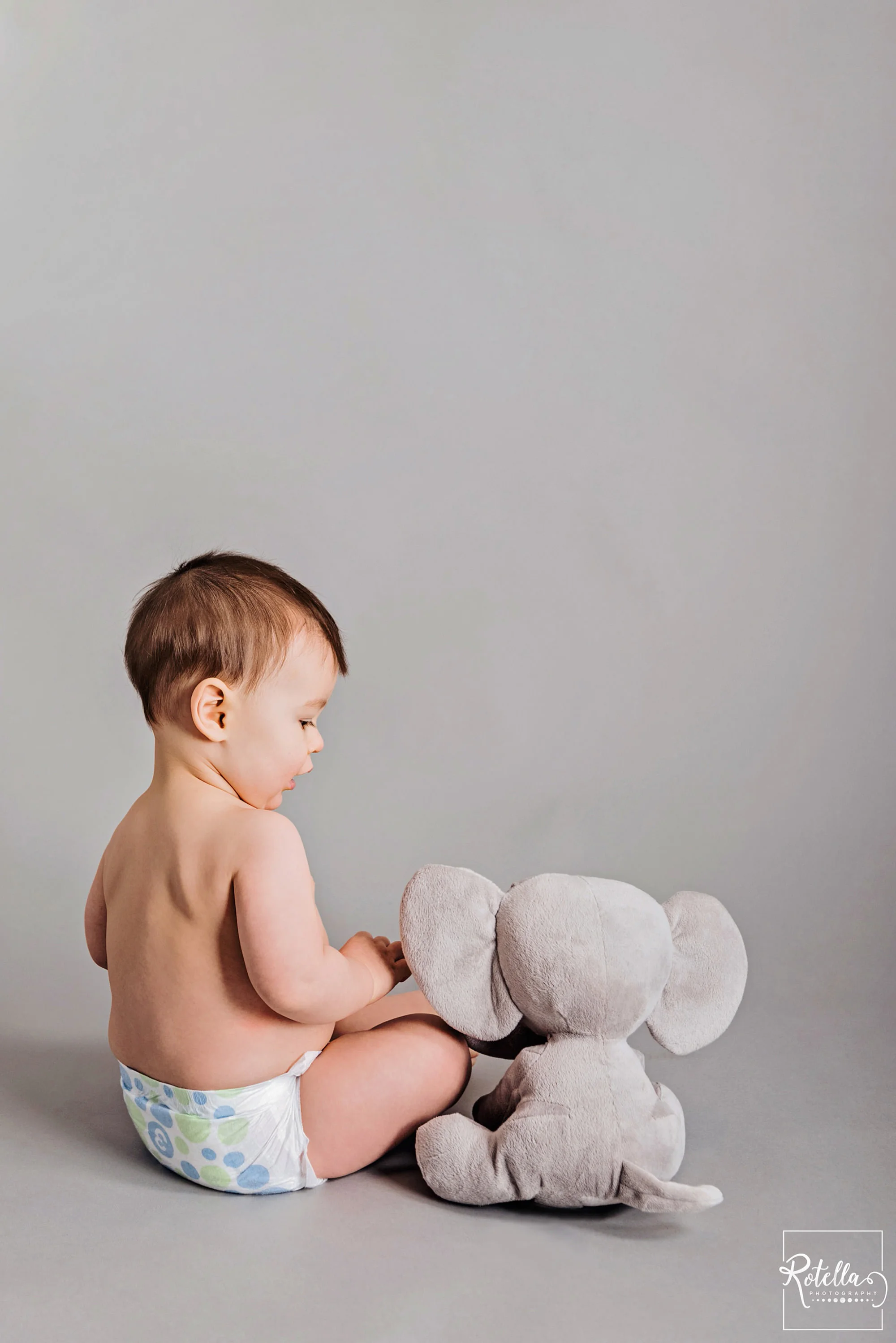 Rotella Photography - milestone photography baby playing with stuffed elephant in studio on grey backdrop