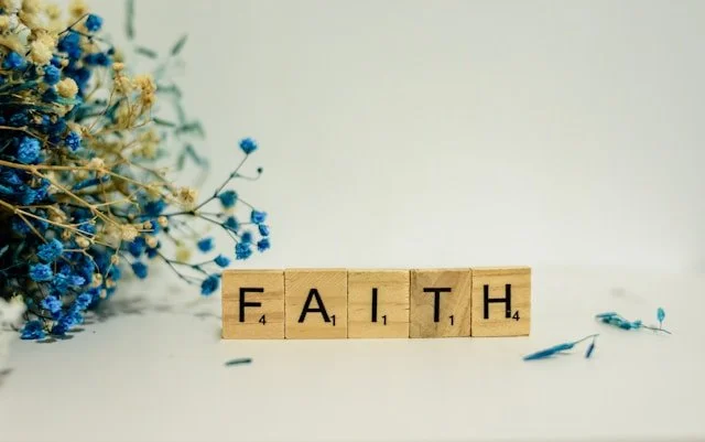 The word "faith" on a white surface next to blue flowers