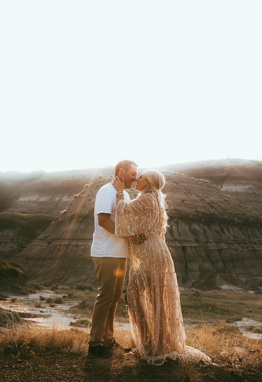 Couple during a golden hour maternity photoshoot in the Alberta Badlands near Drumheller, with soft desert tones, open landscape, and warm natural light creating a romantic and timeless feel.