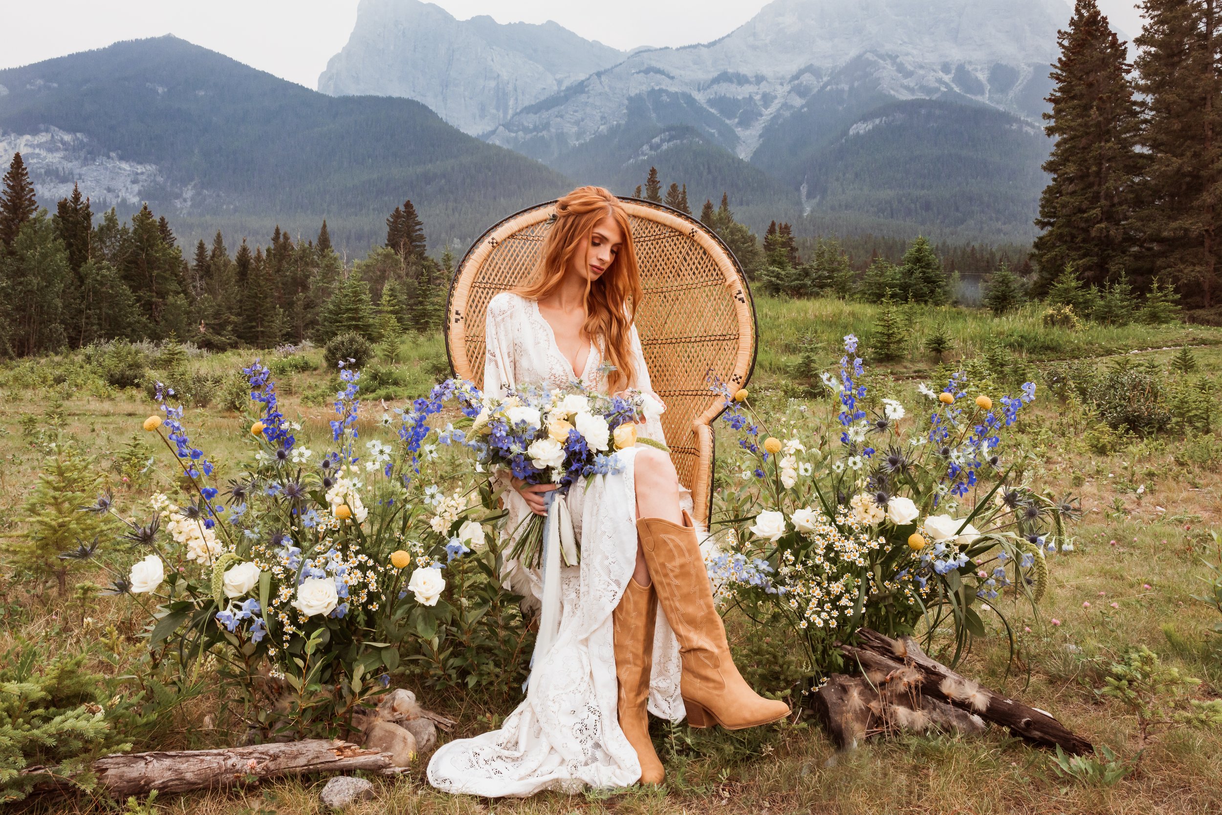 Boho bride in a lace wedding dress and cowboy boots surrounded by wildflowers in the Alberta Rocky Mountains, inspiration for an adventurous mountain elopement.