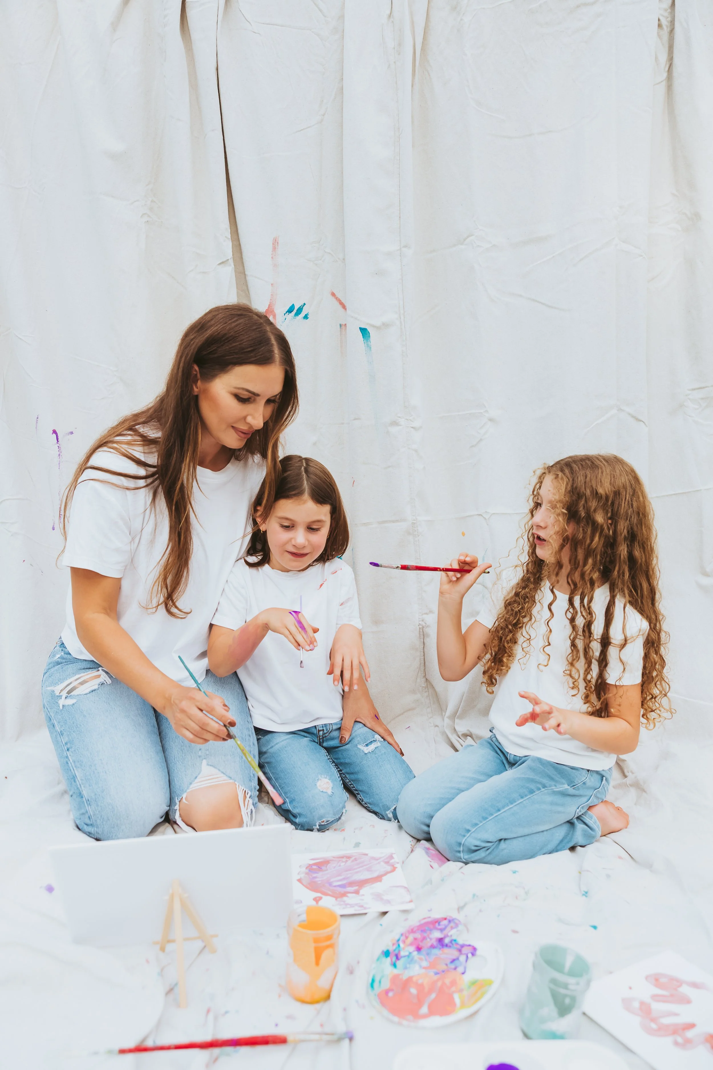 Mother cuddling her daughters during a playful Alberta paint mini session with emotional storytelling family photography and artistic candid interaction.