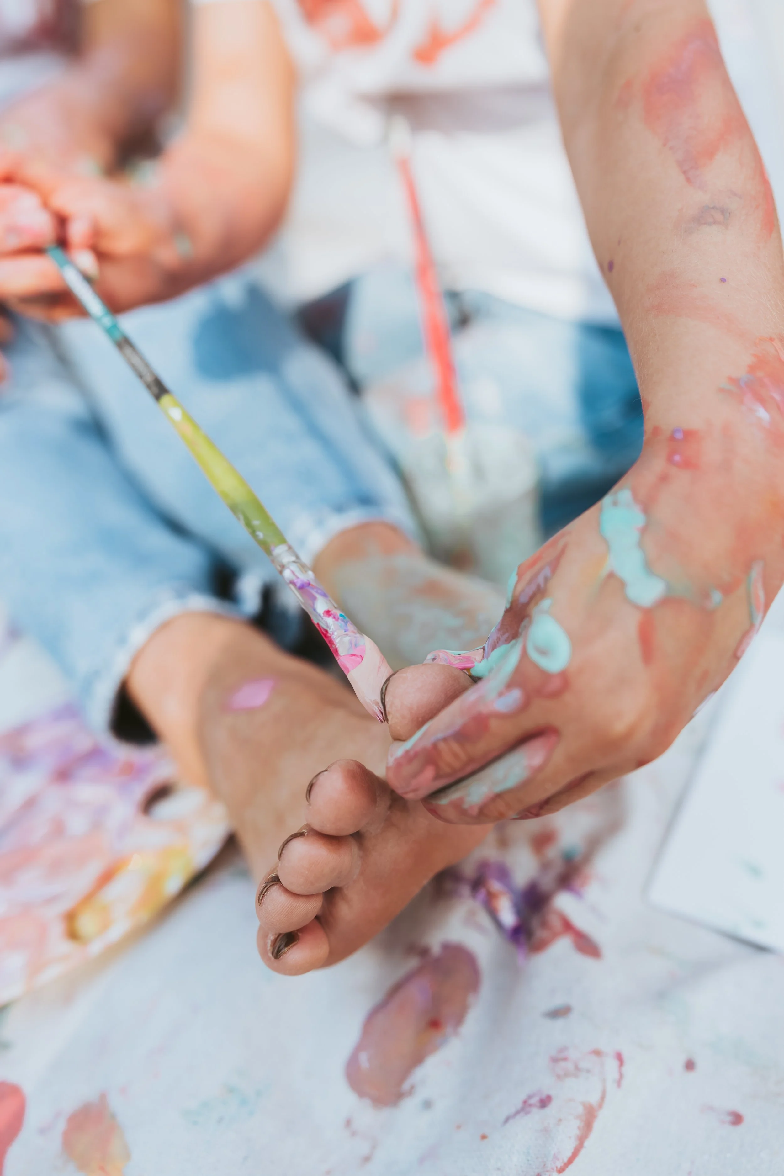 Close-up detail of paint-covered feet and paintbrushes during an artistic Alberta family paint mini photography session.