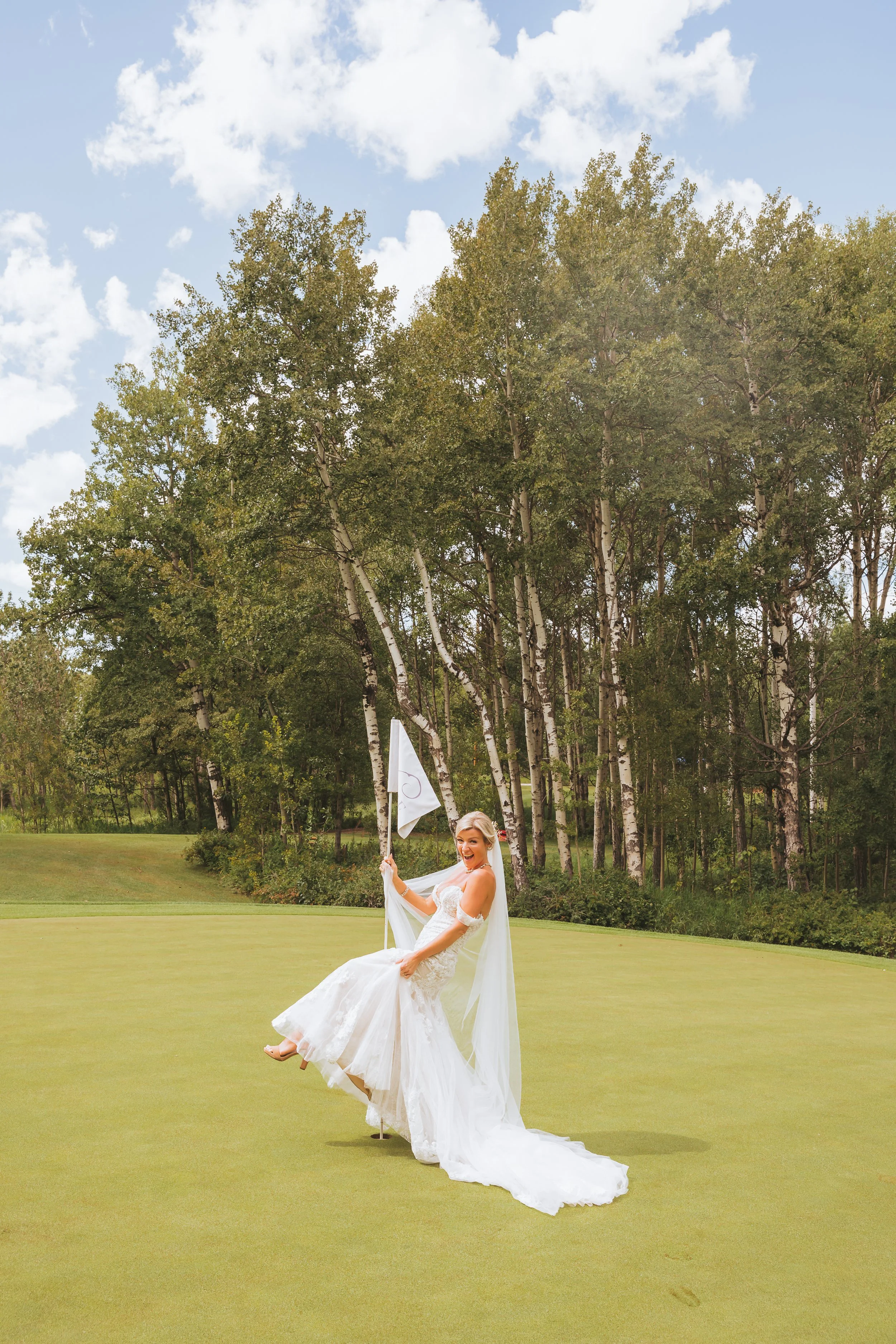 Bride celebrating on a Calgary golf course during her wedding day, showing a playful alternative to traditional wedding photography.
