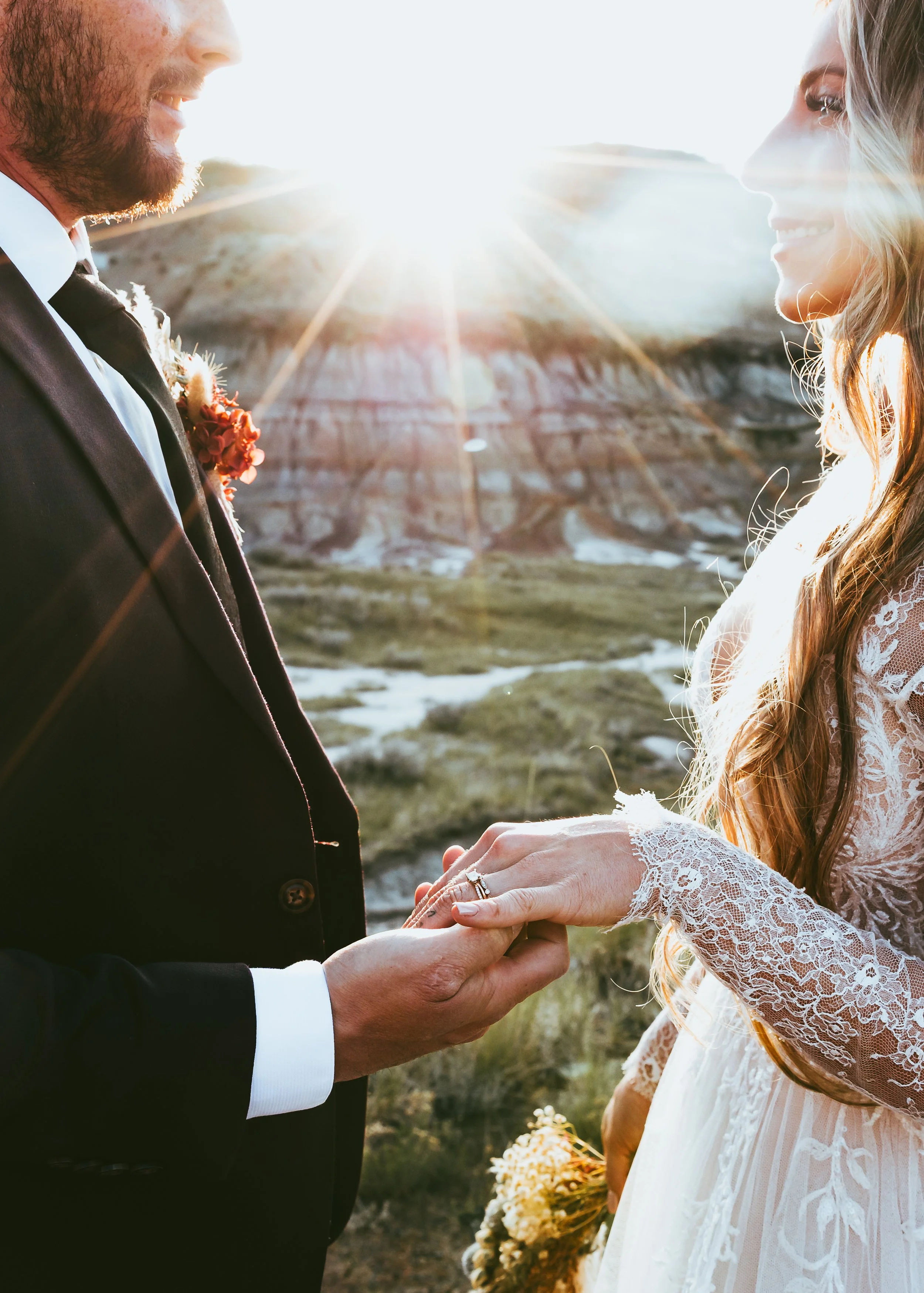 Close-up of a newlywed couple holding hands and showing their wedding rings at sunset in the Drumheller Badlands, Alberta.