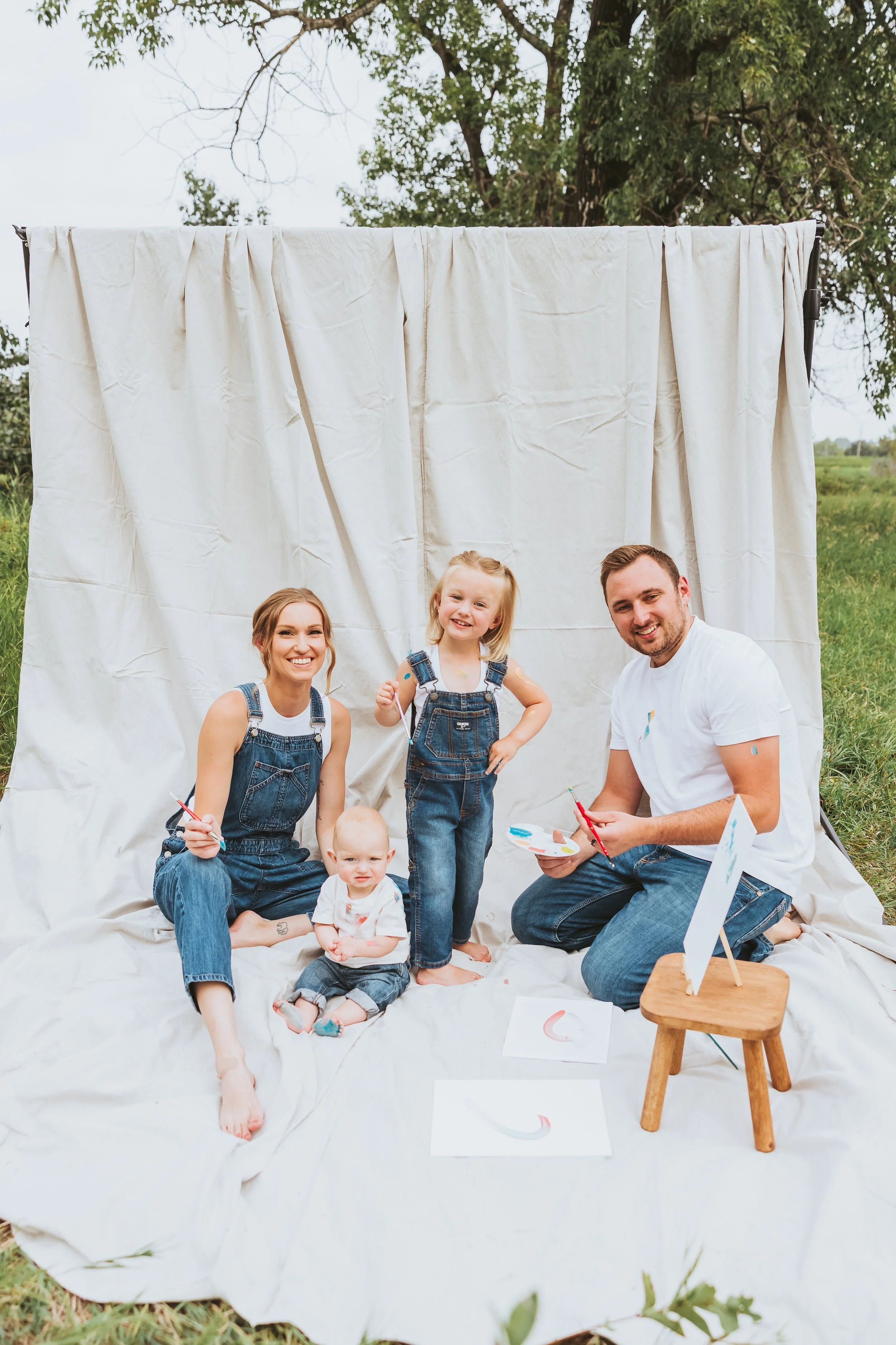 Family painting together during an outdoor Alberta paint mini session with denim styling, playful interaction, and emotional storytelling photography by Maxine LaGarde Photography.