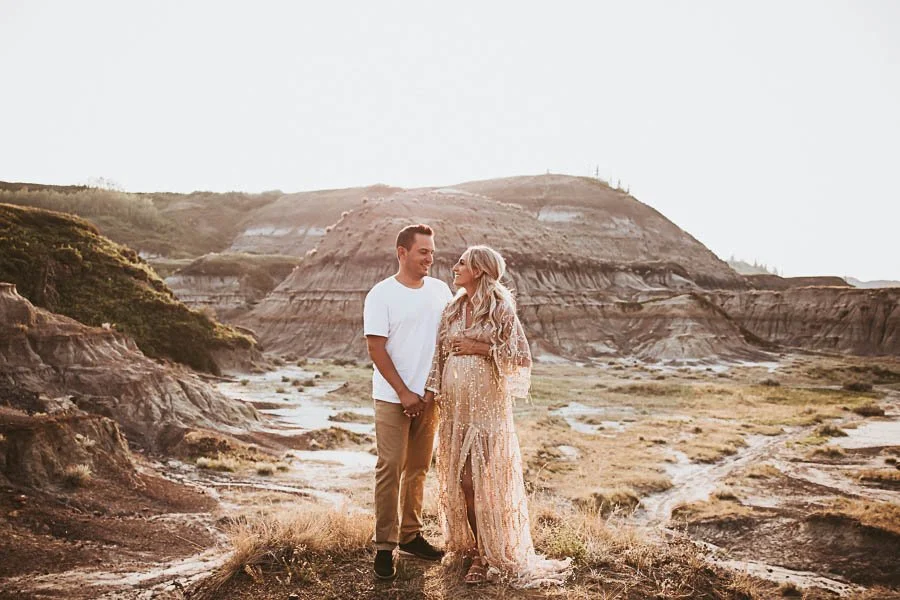 Outdoor maternity photos in the Alberta Badlands featuring a couple embracing on a scenic ridge with golden hour light and open landscape.