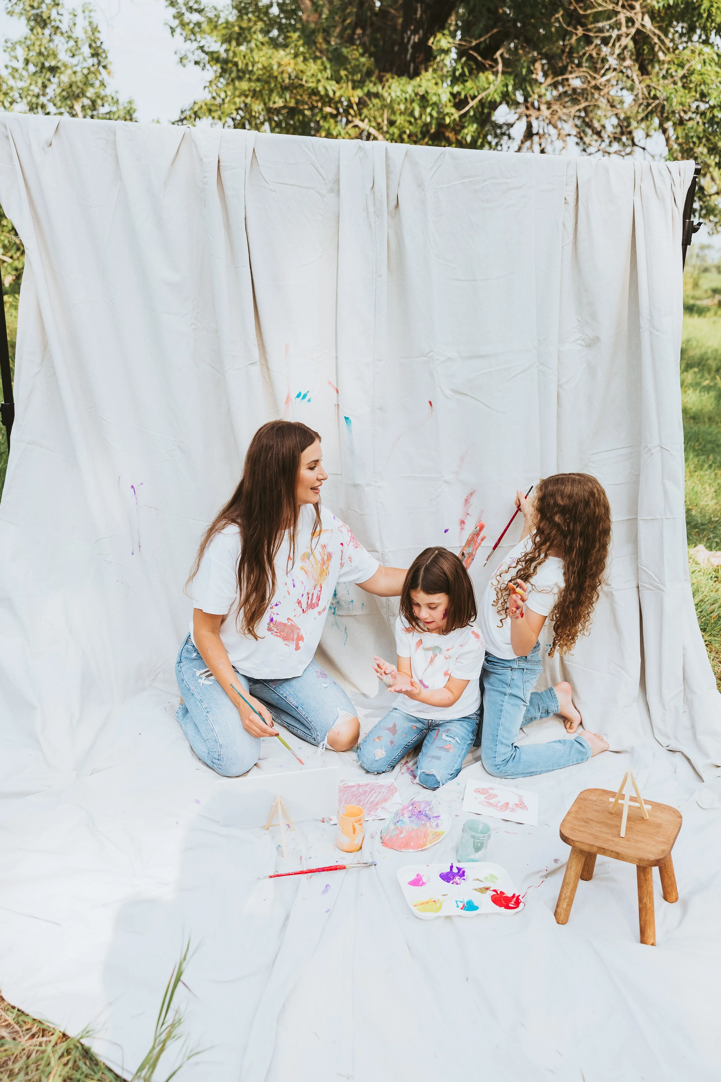 Mother playfully painting with her two sweet daughters in matching light denim and white t-shirts for a creative and stress free photo session in Calgary Alberta.