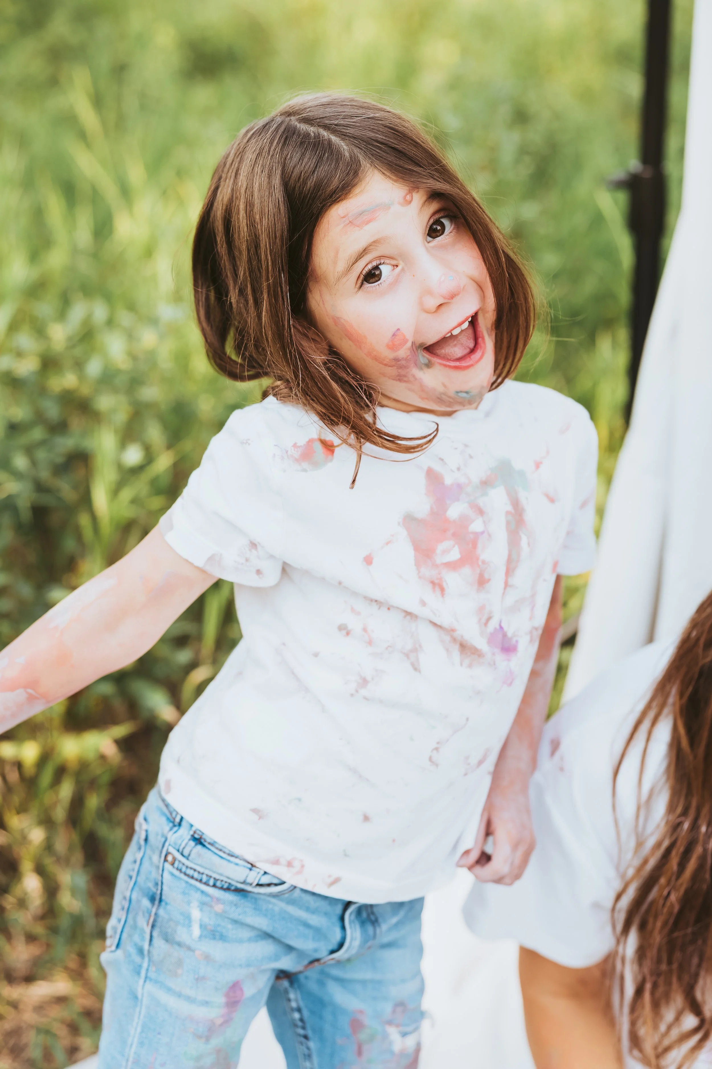 Playful child posing with paint stained clothing in creative art and paint photos sessions in Alberta.