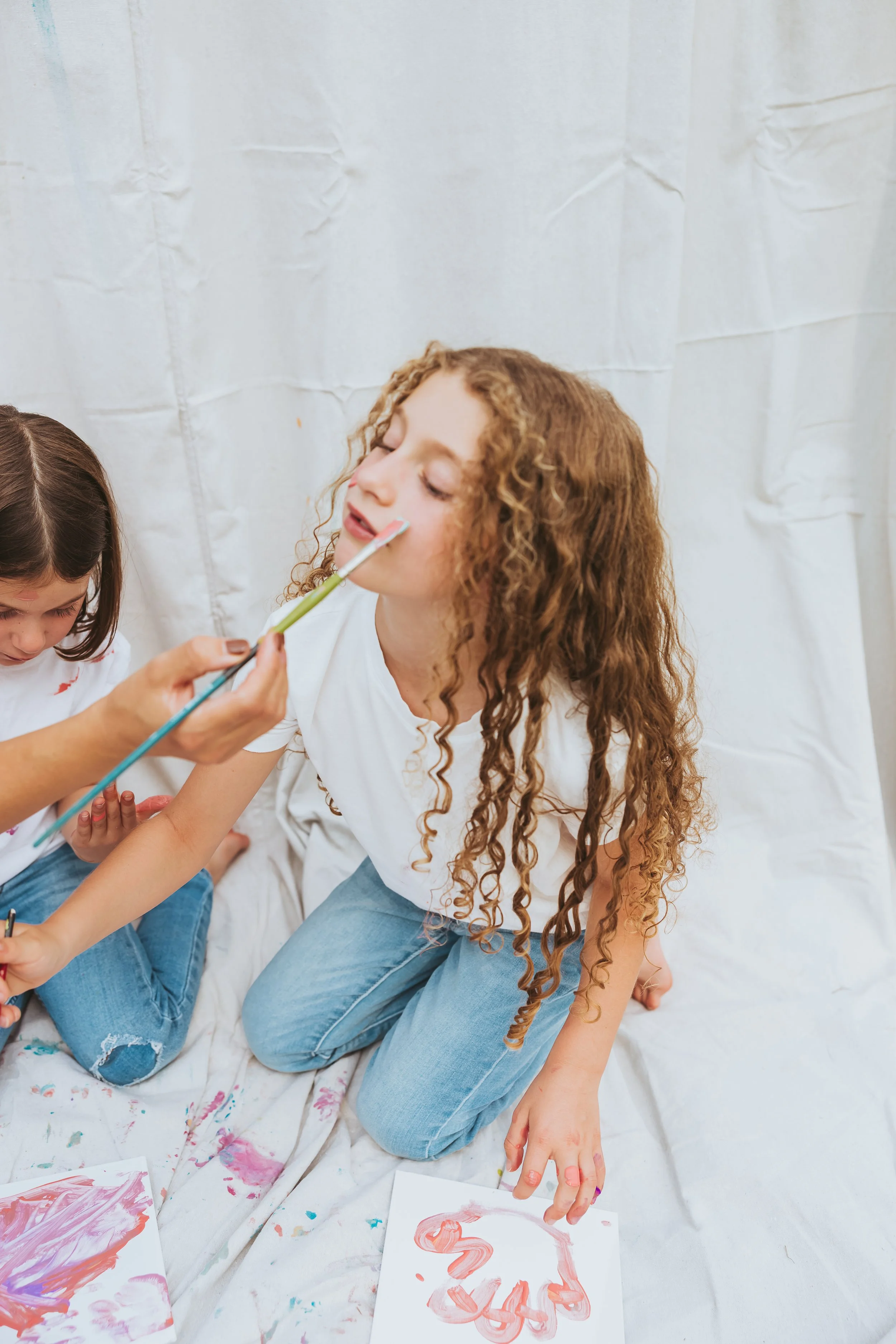 Girls with paint-covered cheeks during a creative family mini paint photo session in Alberta with candid emotional interaction and playful storytelling moments.