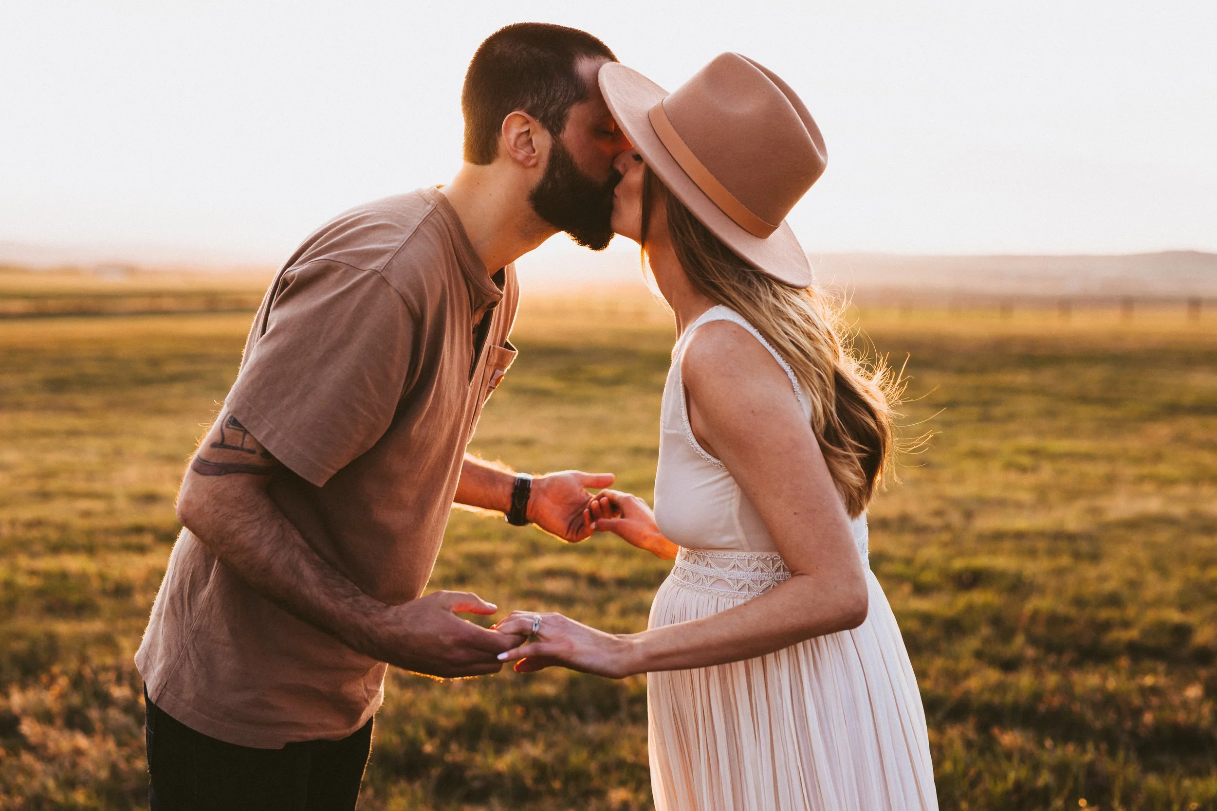 Expecting couple sharing a kiss during a sunset maternity session in an open field, warm golden light
