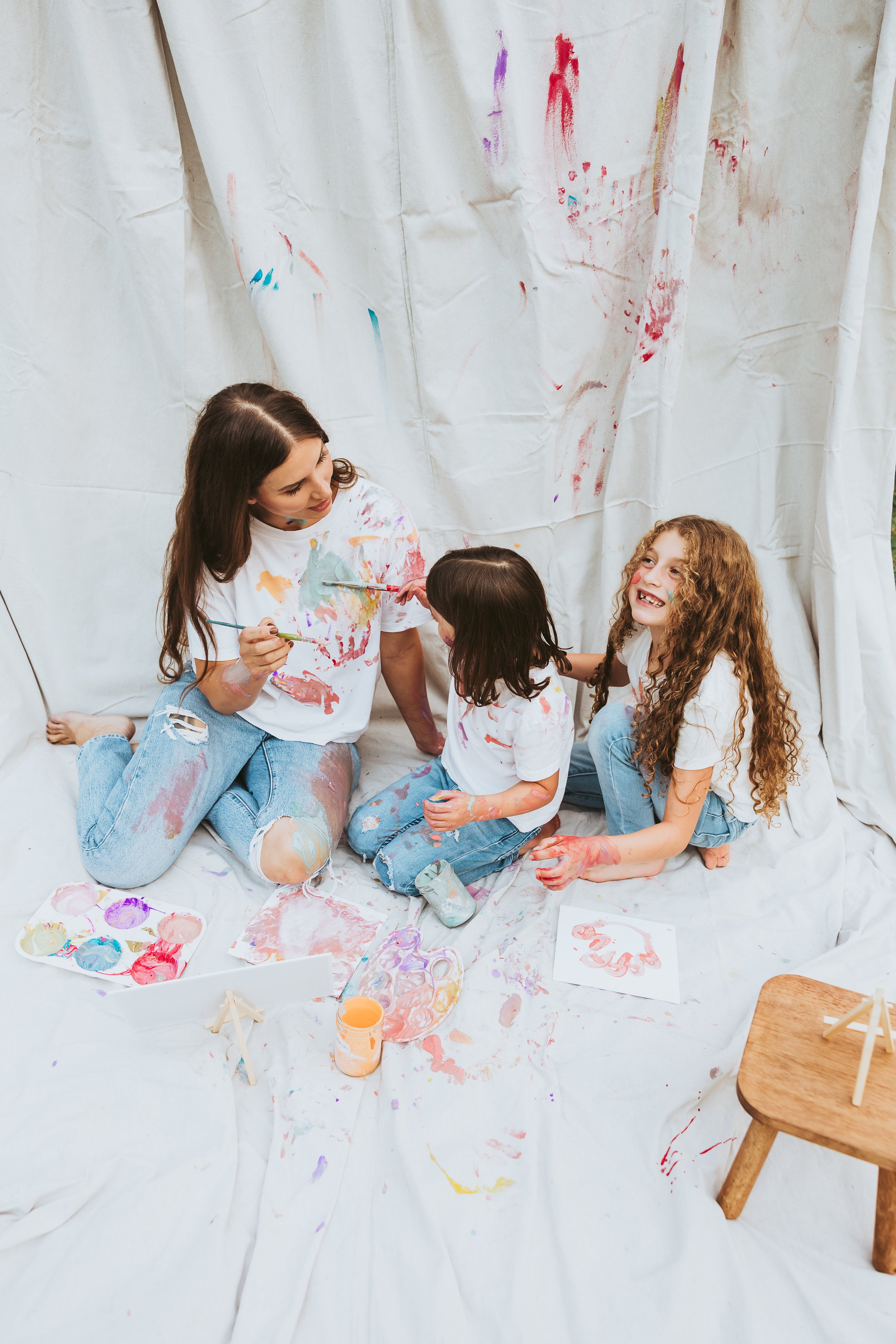 Mother joyfully painting her daughters during a playful Alberta paint mini session with emotional storytelling family photography and artistic candid interaction.