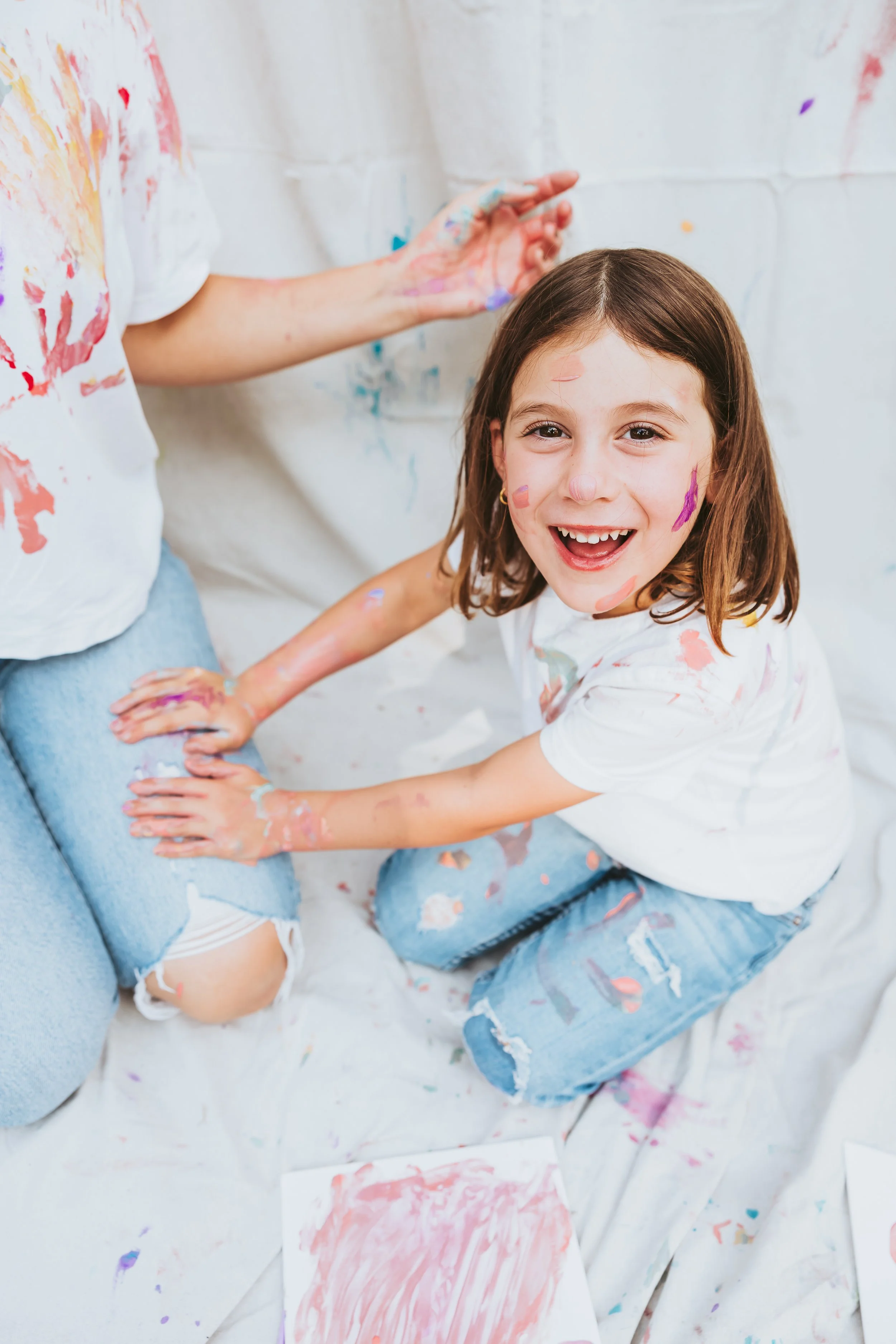 Playful mother and daughter dressed in light denim and white t-shirts make art while enjoying a relaxed and creative paint mini photo session in Calgary Alberta park.