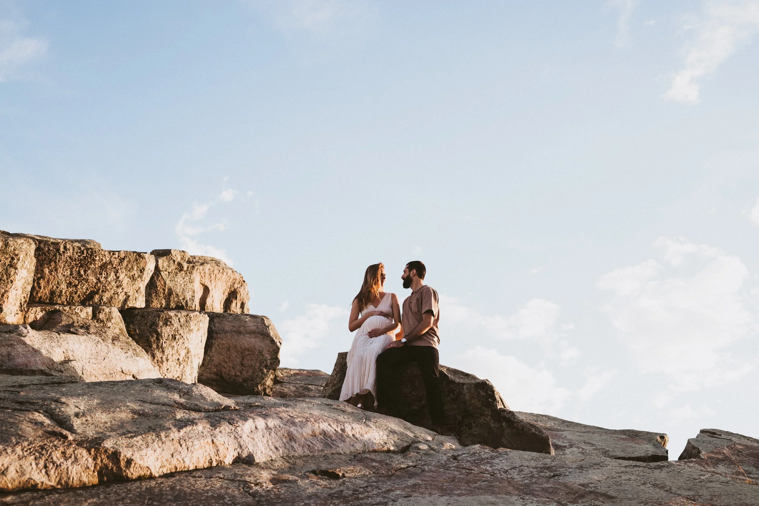 Expecting couple sitting together on rocky cliffs in the Alberta Badlands during a sunset maternity photography session