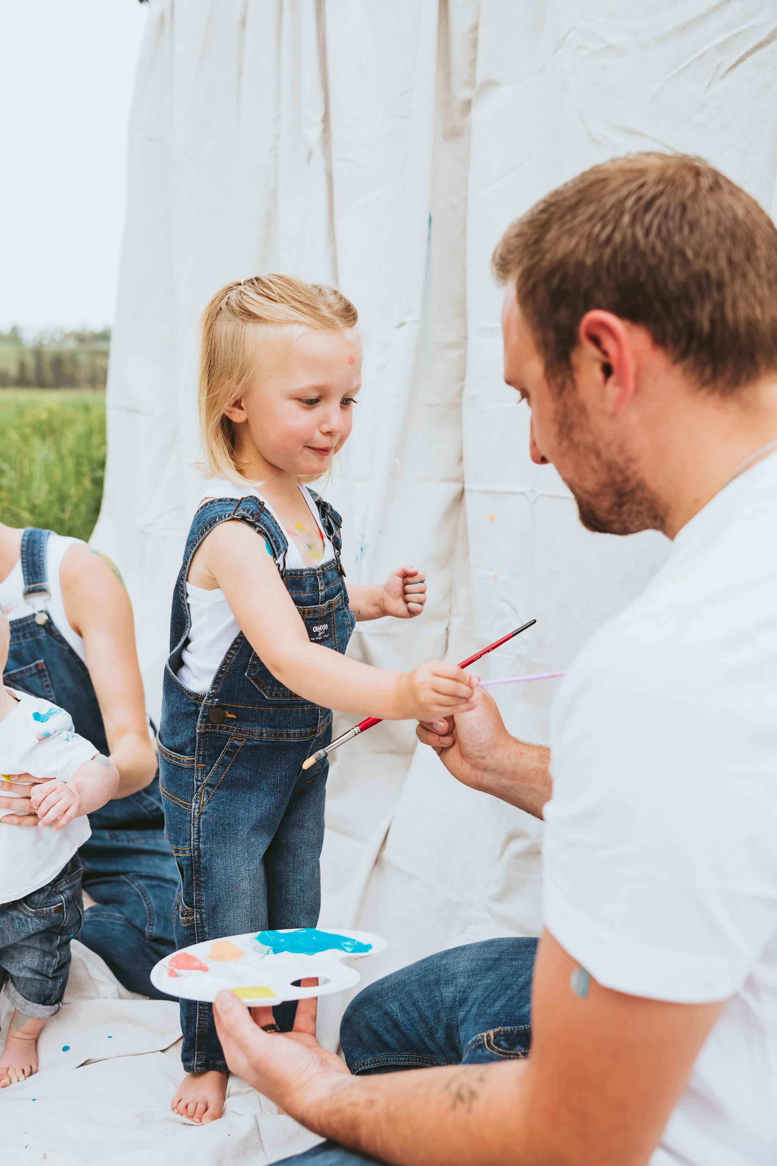 Father and daughter painting together during an outdoor Alberta paint mini session with denim styling, playful interaction, and emotional storytelling photography by Maxine LaGarde Photography.