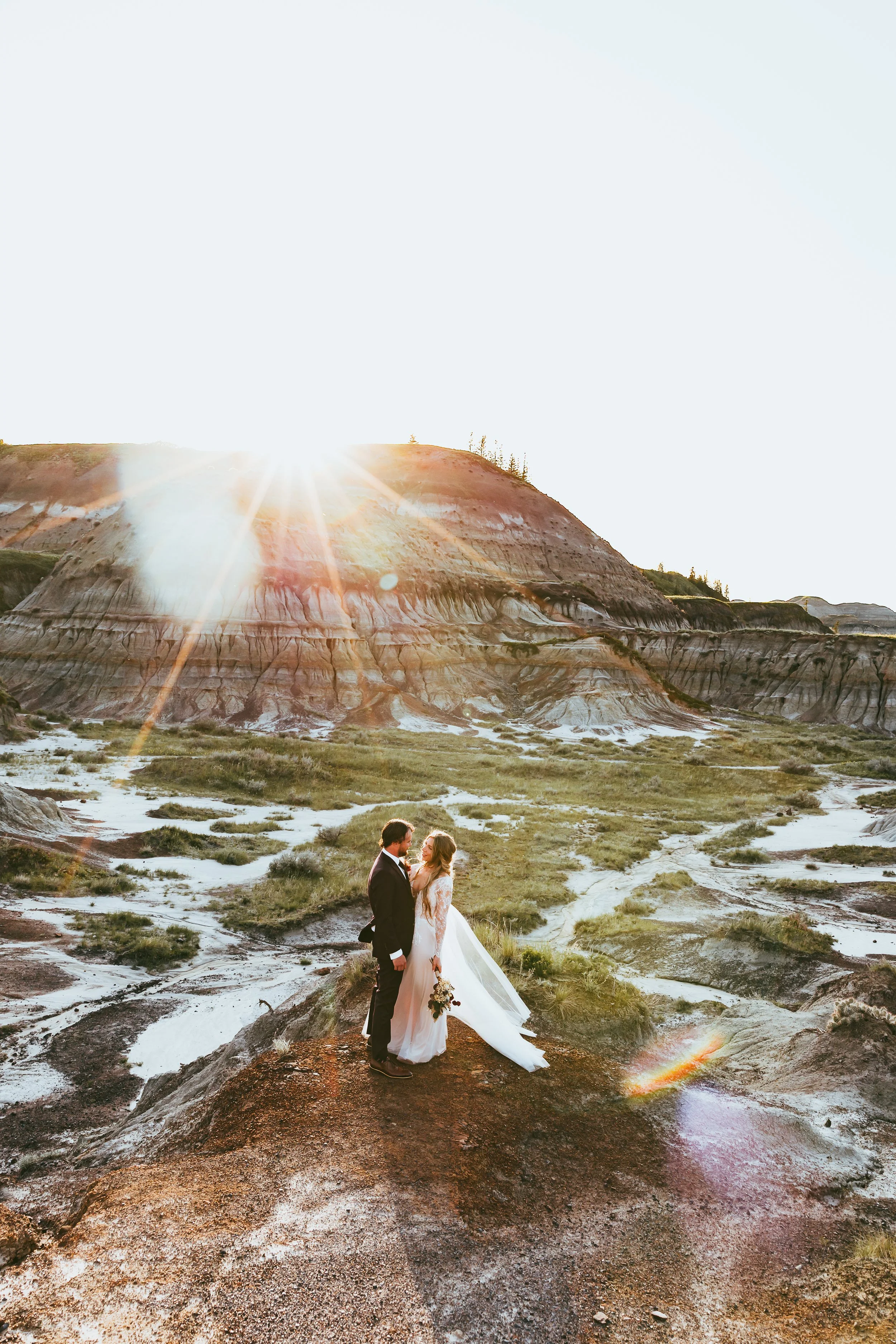 Joyful bride hugging groom during golden hour sunset in Drumheller Alberta Badlands with glowing backlight backdrop.