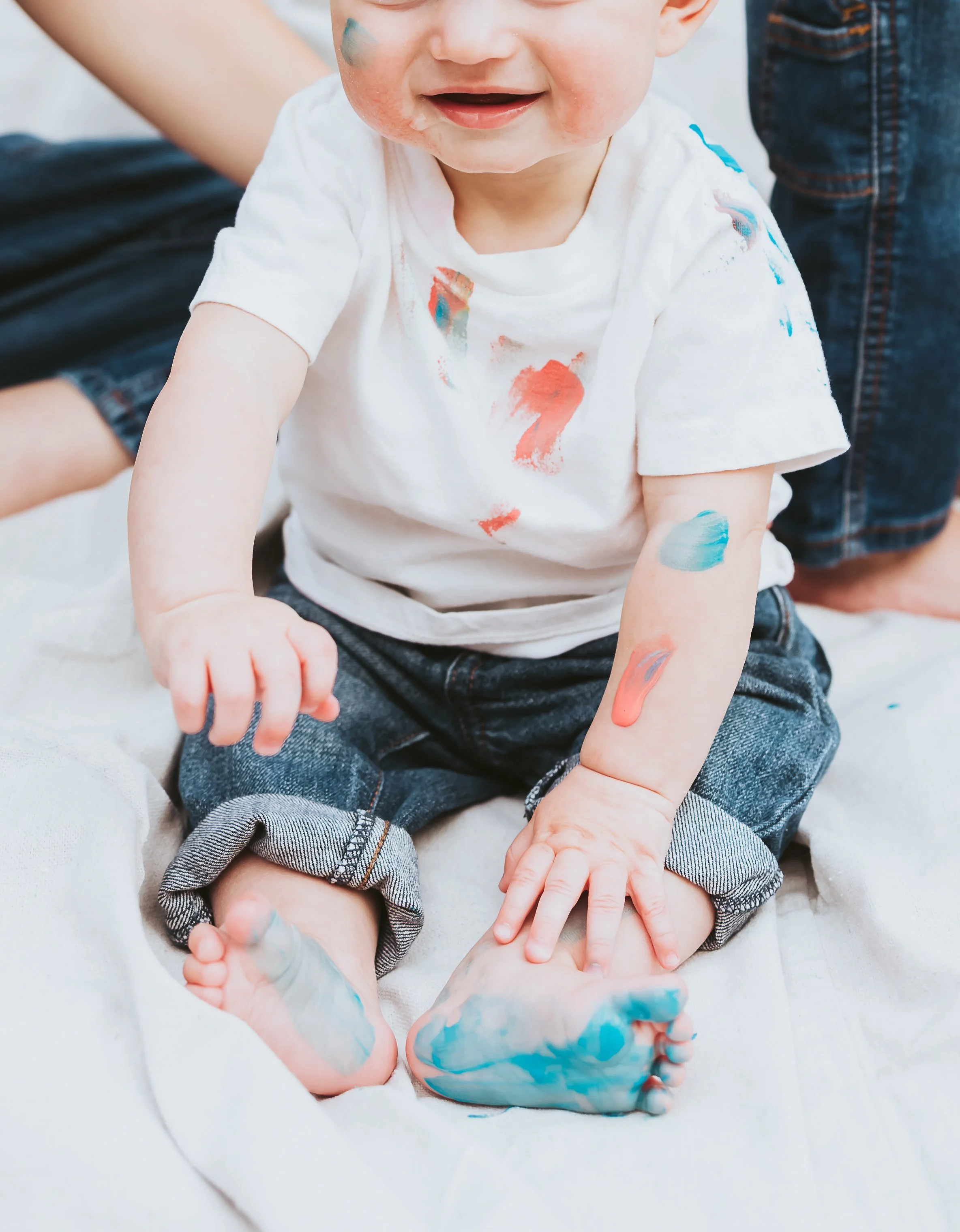 Baby smiling during a playful Alberta paint mini session while sitting in mother’s lap wearing denim overalls and white neutral styling by Maxine LaGarde Photography.