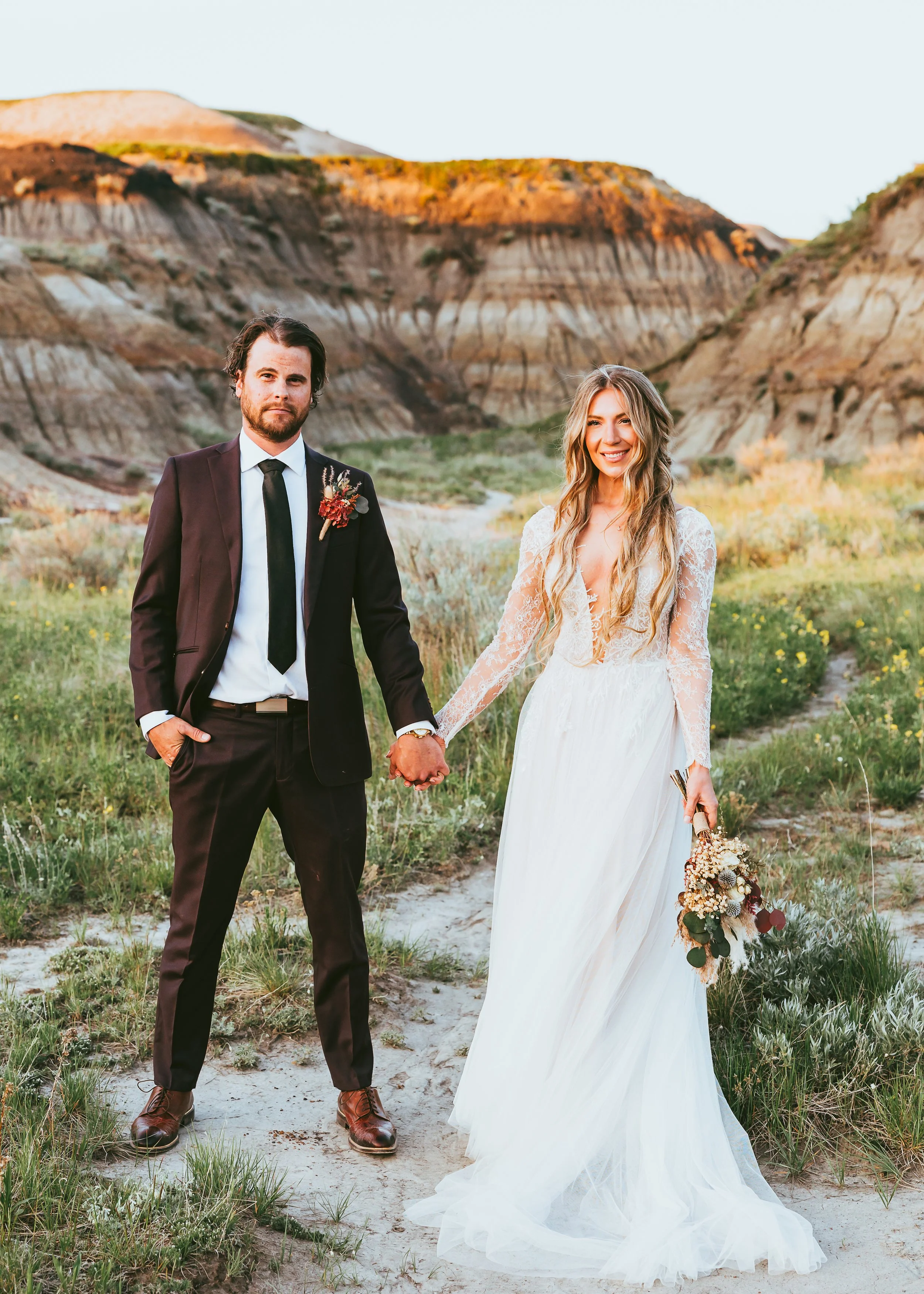 Full body bride and groom portrait in Drumheller Alberta Badlands with soft natural light and textured landscape background