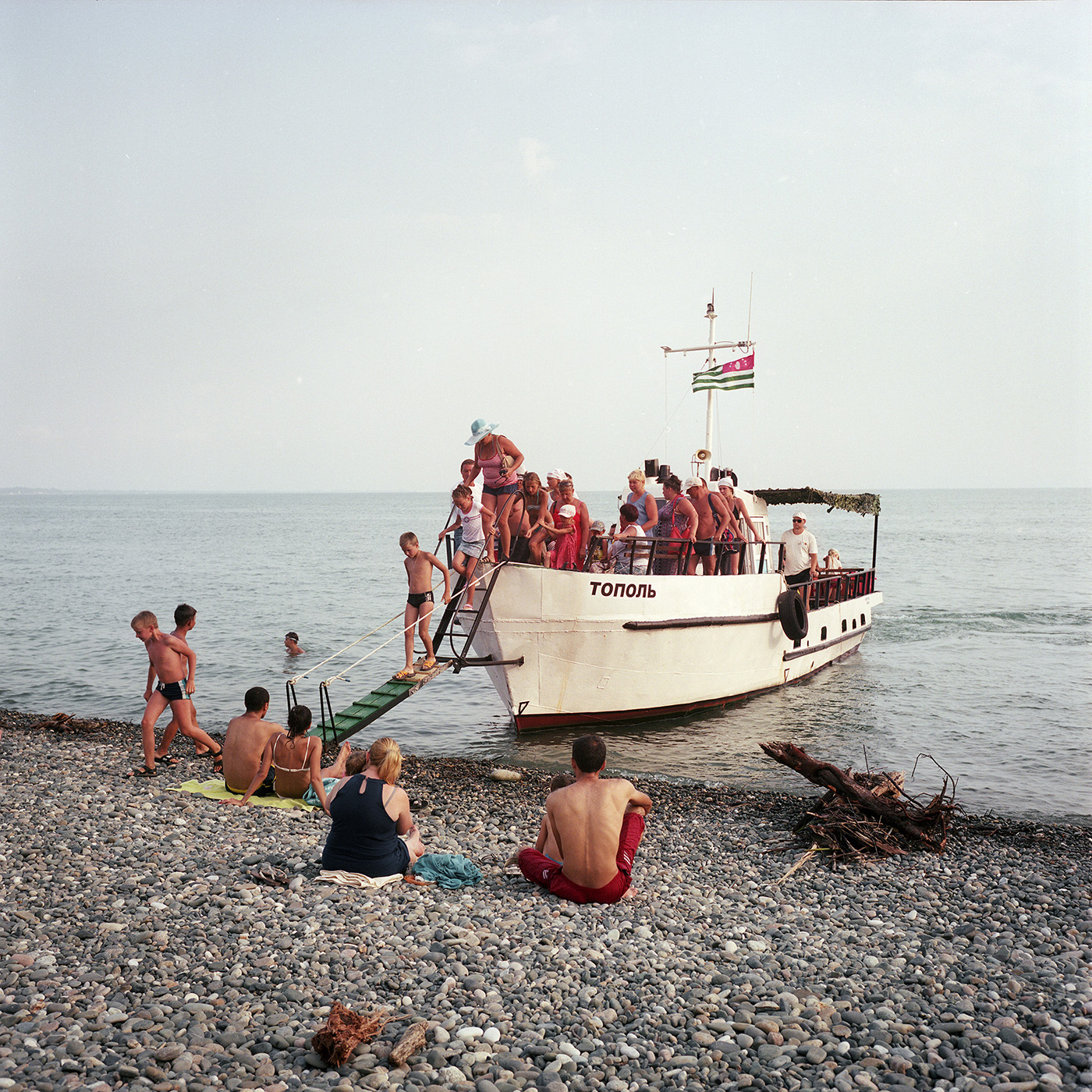  On the beach in Gagra. A boat comes take the tourists for an hour trip. The boat's captain was working on large fishing vessels in the past. Today, he renovated this boat and works for tourists. 