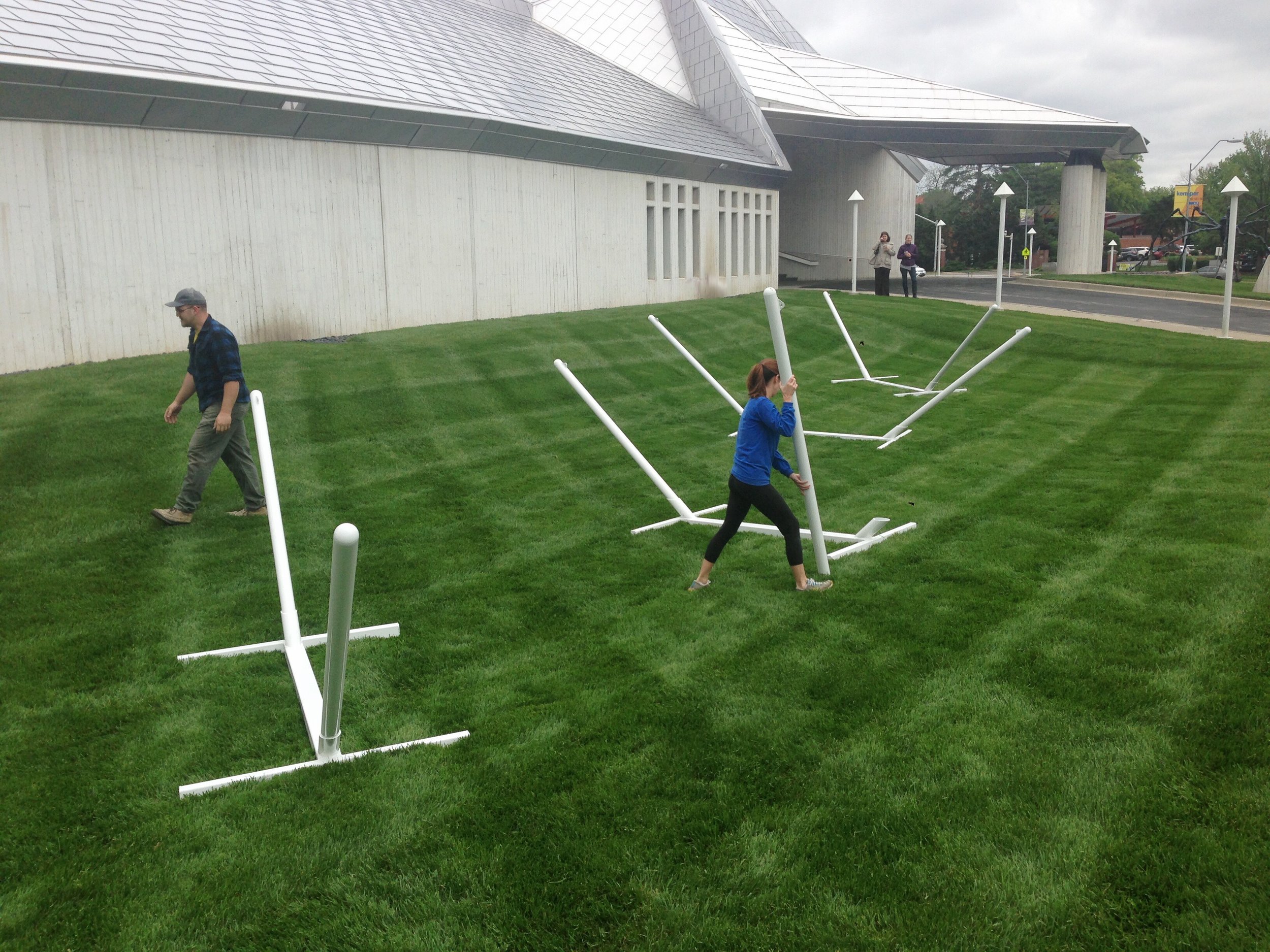 An installation photo shows that the design of the hammock stands allows for the burial of the connecting support base to maintain an elegant minimal appearance as well as insuring that the space directly below the hammocks is open to the soft turf in case users tumble out.