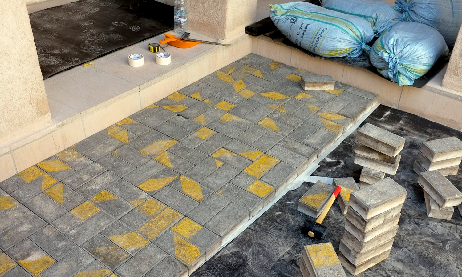    Degenerative Disarrangement ,  2013  Pavement bricks with parallel yellow marks are removed from a site. At the exhibition site a hired mason installs the bricks within demanding time constraints workers regularly face, resulting in arbitrary patt