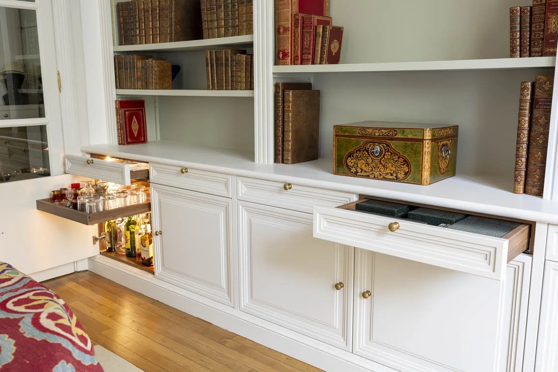 Un espace bar caché mais bien pratique. Dans un des placards, nous avons créée un bar avec tiroir coulissant et lumière intégré. Une façon agréable mais discrète de présenter bouteilles d’alcool et verres.