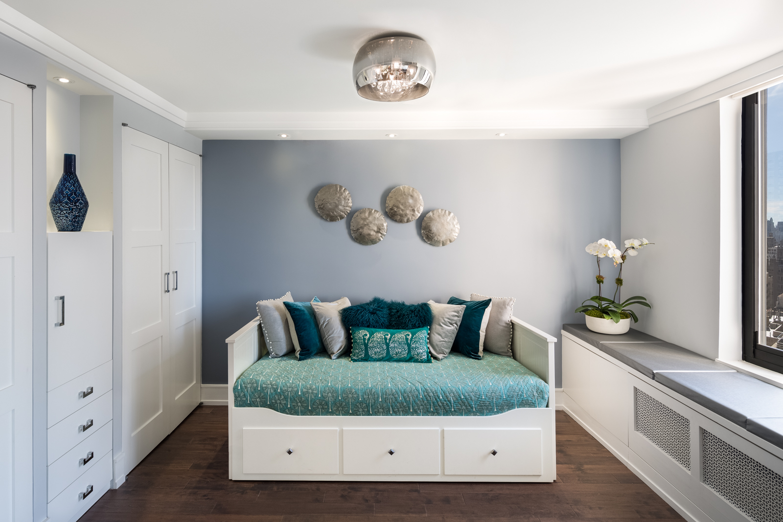 The multipurpose room is an extension of the living room with the overall color palette of grey, blue, silver and white. The room also is a music room for the violinists in the family (unfortunately not pictured here), a guest room for when family visits (this daybed opens into a king sized bed), mom's office everyday (shown in next pic) and the perfect spot for reading or watching the snowflakes dance. The custom window seat cushion has minimal banquette-like style in faux leather for easy maintenance. The custom grille hides the unsightly air conditioner which we were not allowed to touch by the building. 