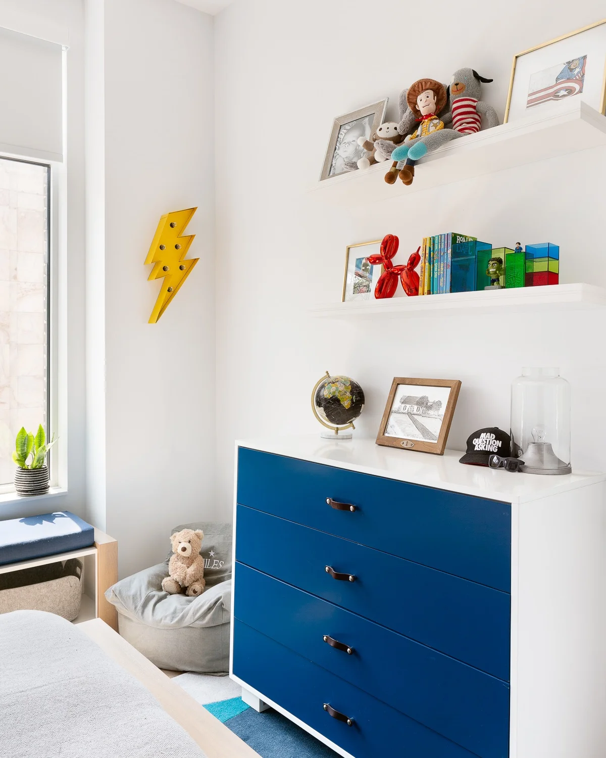 Beautiful custom dresser with leather pulls create much needed storage and style on the other side of the room against a simple painted wall. The accent lightning bolt marquee light brings the super-hero theme and floating shelves above create space for rotating gallery of art, toys and of course books. Felt baskets provide easy access to toys, blankets and more books for our little reader.