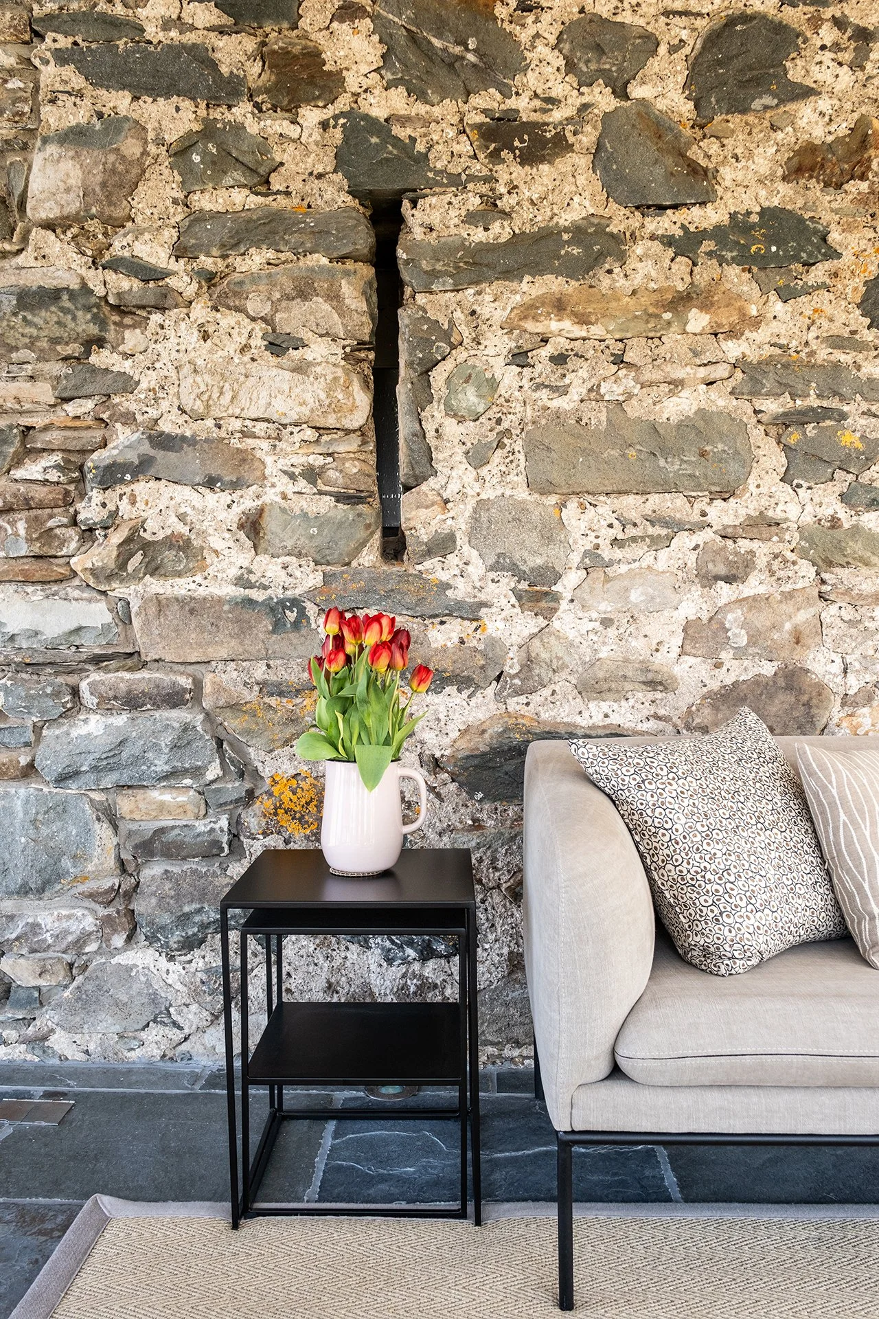 interior design remodel by luxury interior designers uk with upholstered sofa, custom side table, chevron rug, patterned cushions and exposed stone wall
