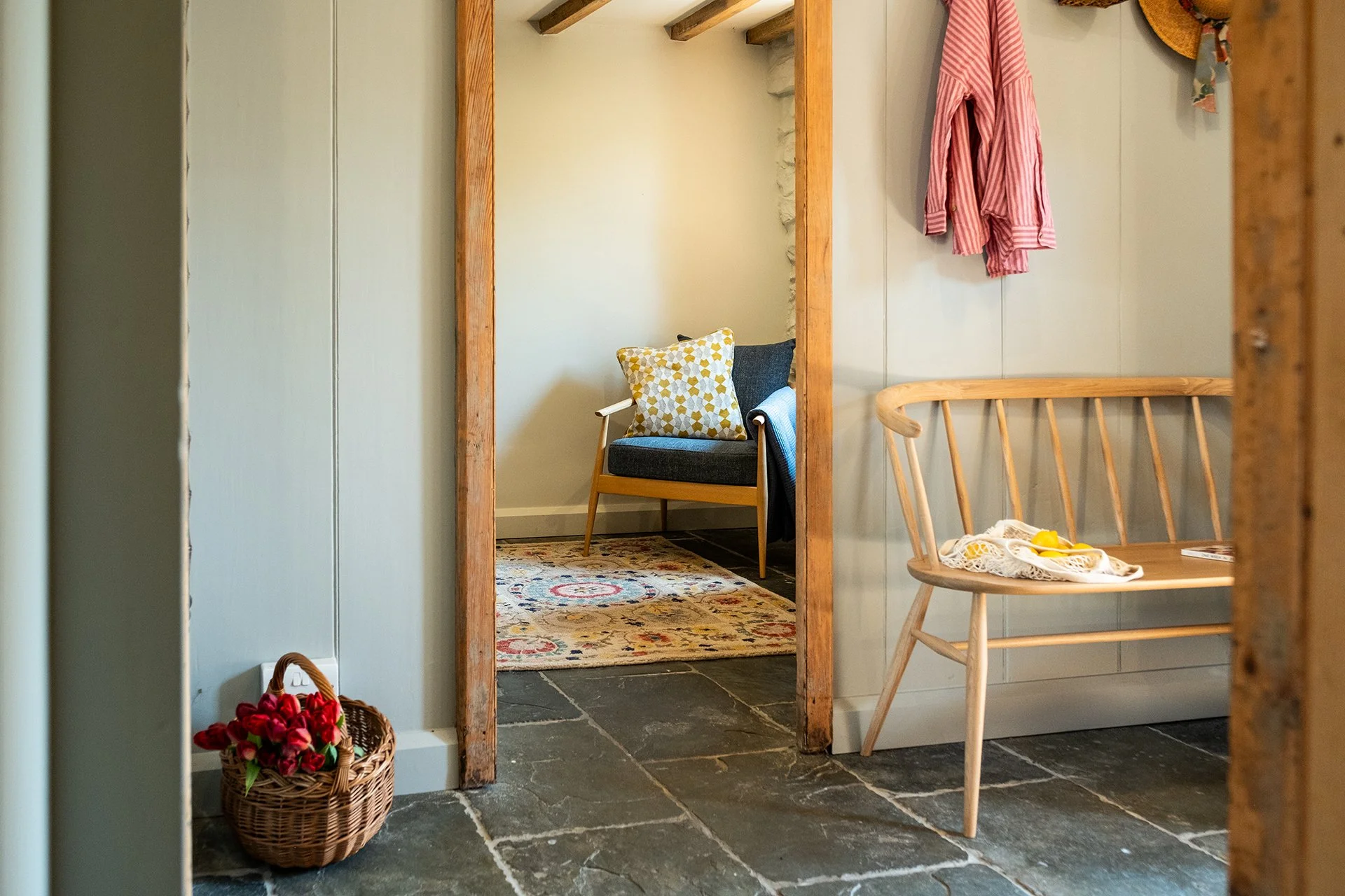 entryway interior design inspiration featuring fabric upholstered armchair, bespoke wooden bench, straw basket, patterned rug, slate floor tiles and wood beams