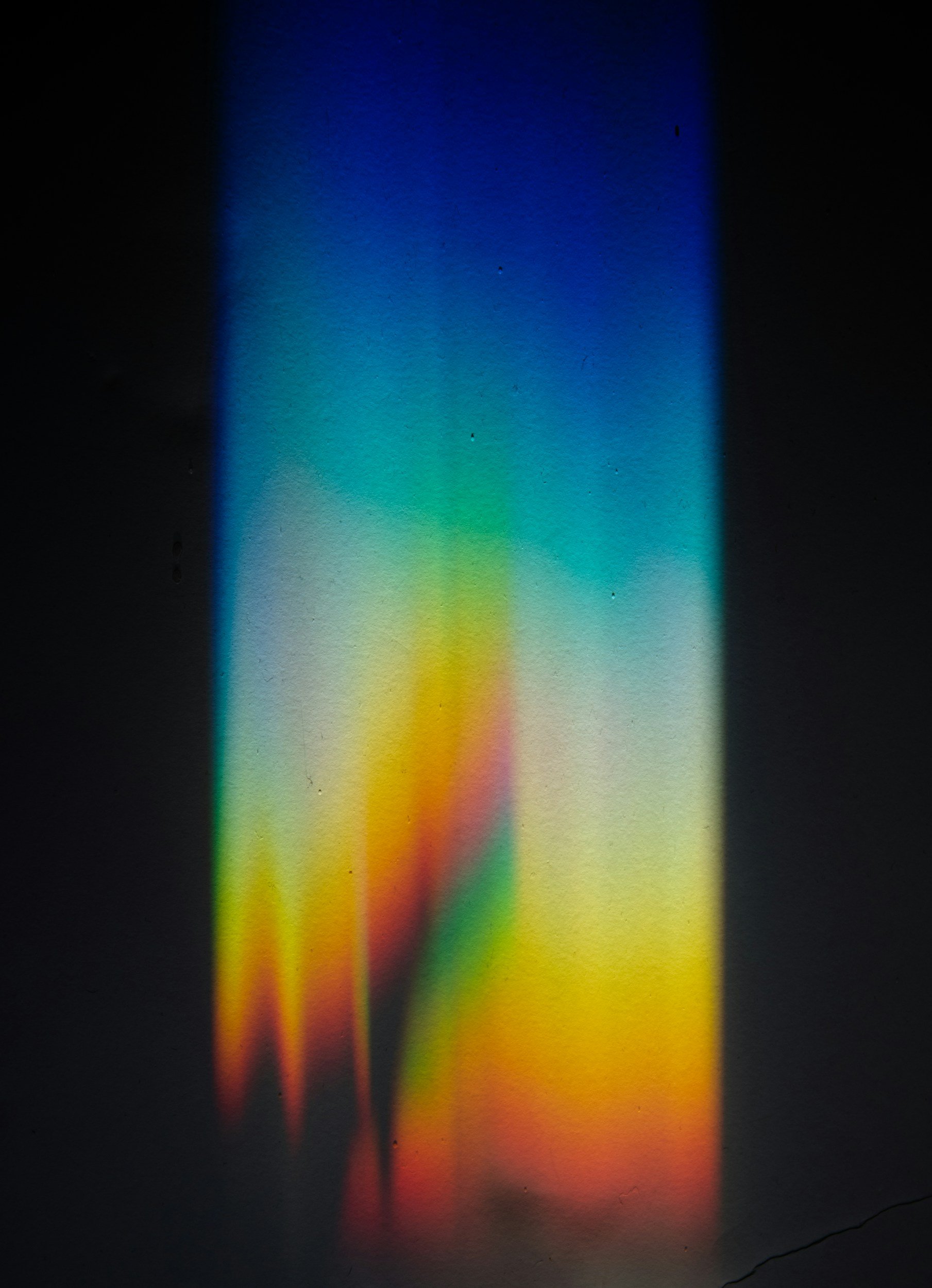 Colorful light projection on a wall with a gradient of blue, green, yellow, and red hues.
