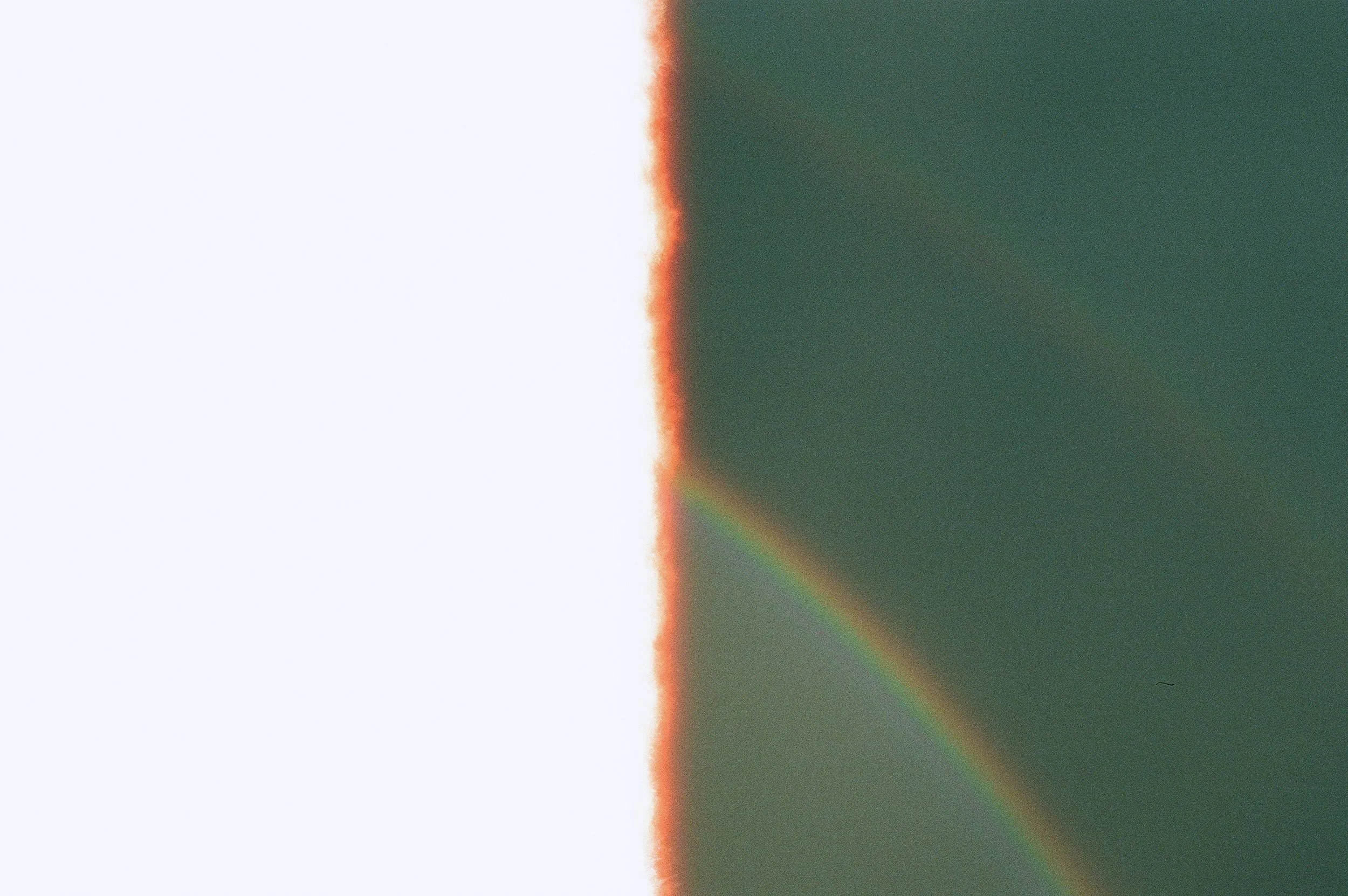 A diagonal split in the image shows a rainbow against a dark sky on the right side and a white or light-colored wall on the left side.