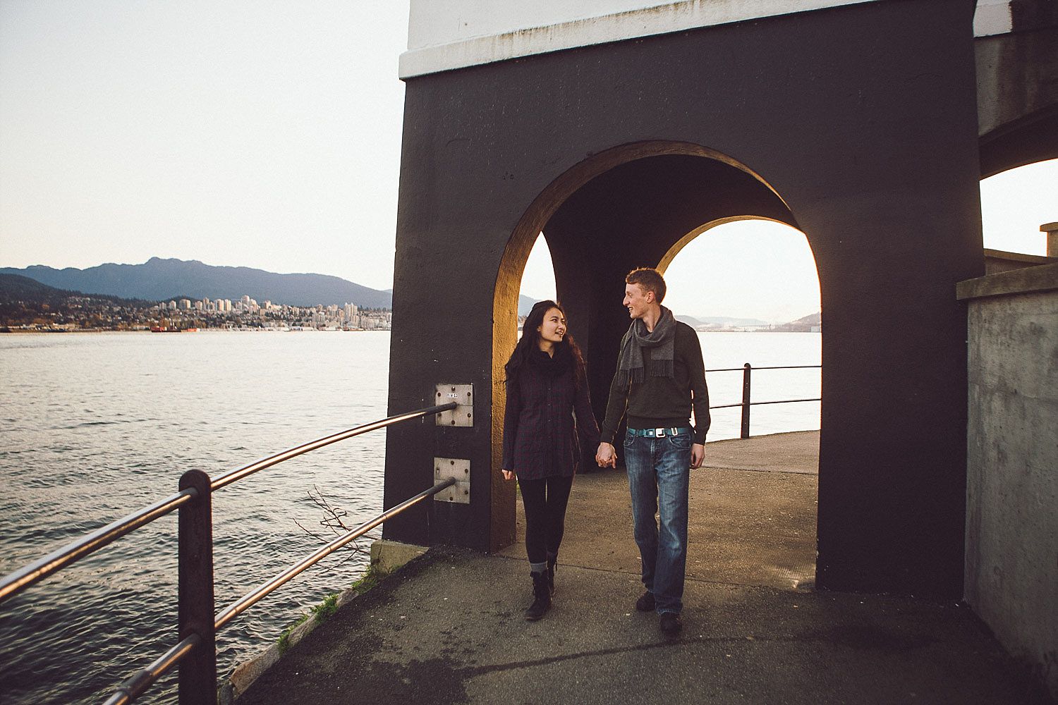  Angel and Tim hold hands as they walk under the arch at the Brockton Point Lighthouse for their engagement session 