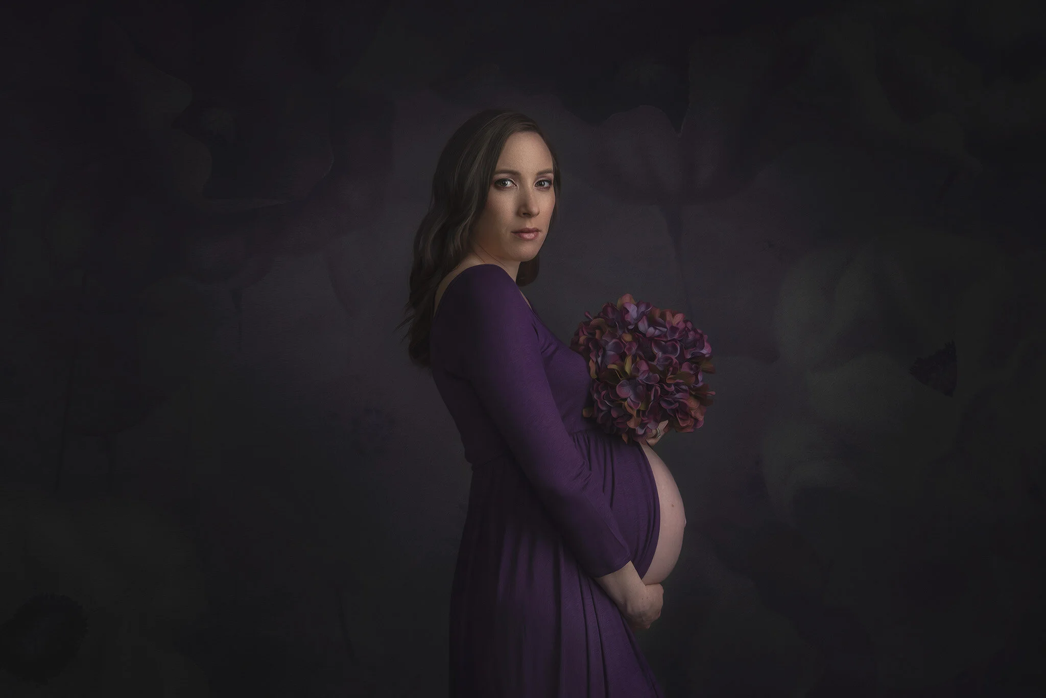 Artistic maternity portrait of a woman in a purple split maternity dress with matching flowers at Fotoplicity studio in East Brunswick NJ