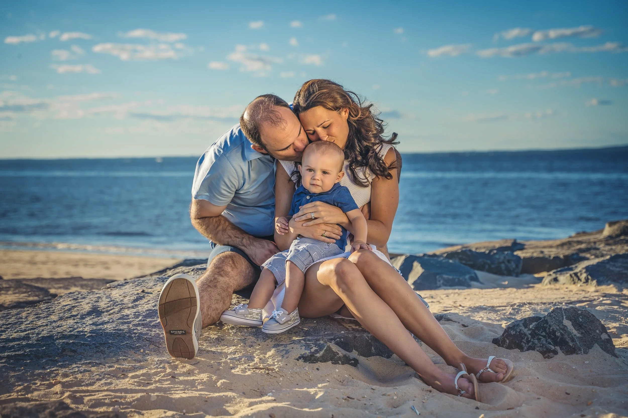 Family of three sitting together on the sand during a relaxed beach family photo session along the New Jersey shoreline.