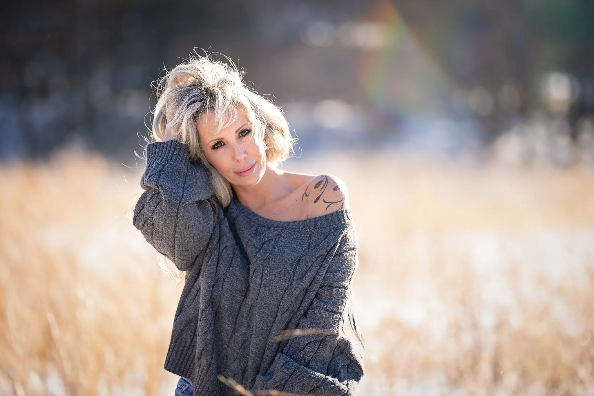 Woman with blonde hair in a grey sweater laughing naturally during an outdoor women's portrait session with Fotoplicity in New Jersey