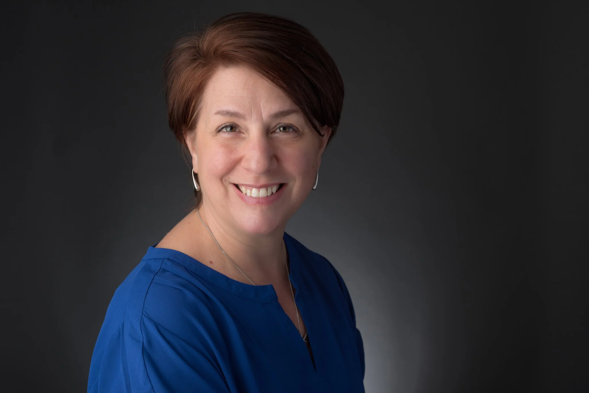 Professional headshot of a woman on a dark gray background, photographed at Fotoplicity studio in East Brunswick NJ